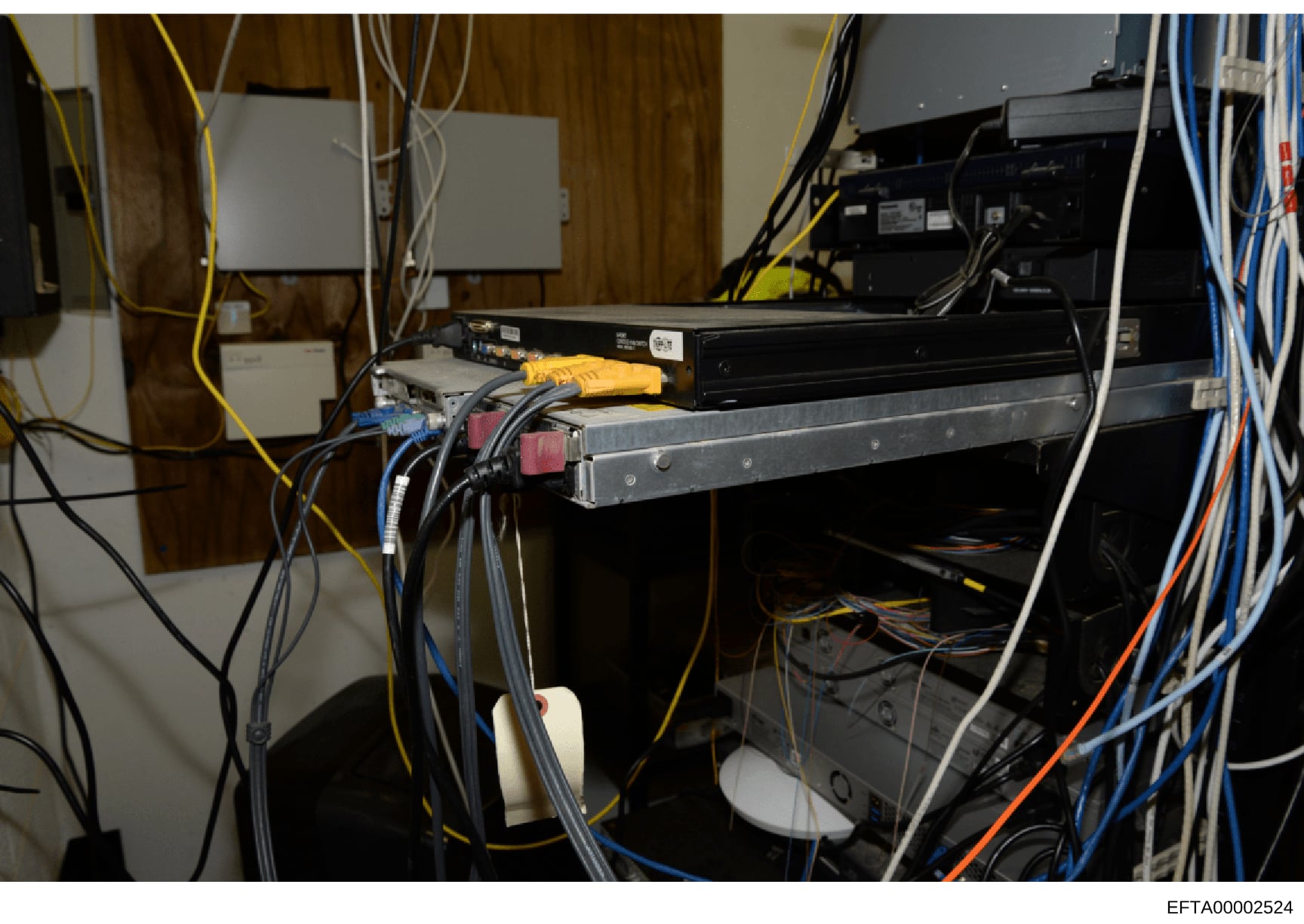This photograph documents a server room or network equipment installation, showing various electronic components including servers, networking devices, and extensive cabling infrastructure. The image captures the technical setup of what appears to be