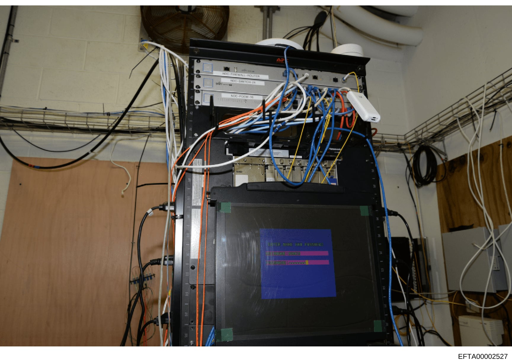 This is an evidence photograph showing a computer network infrastructure setup with multiple server units, network switches, and extensive cabling in various colors (orange, blue, white, black). The equipment appears to be mounted in a rack with a mo