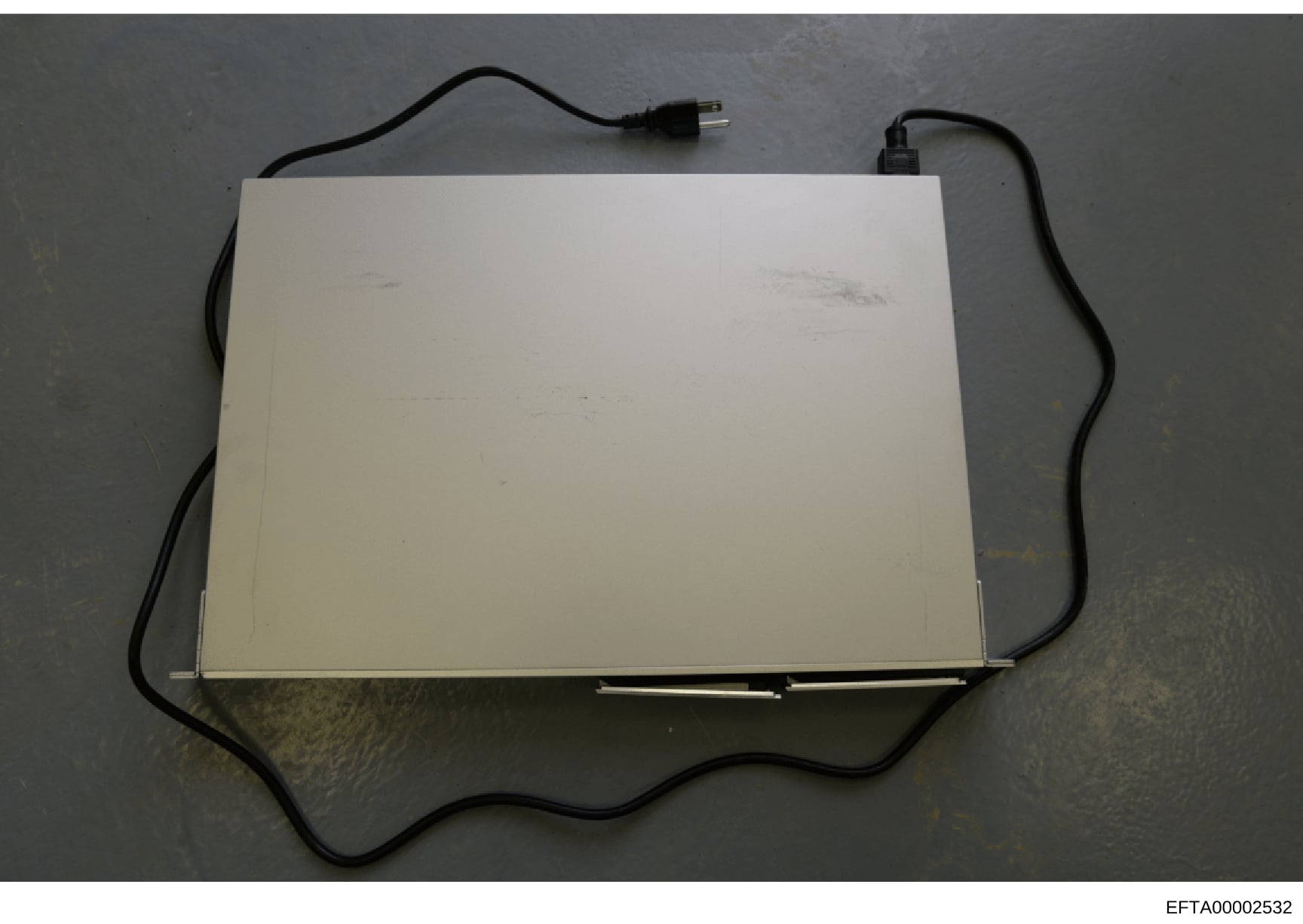 This is a photograph of a light box or similar illumination device with attached black power cables, documented as physical evidence in the Epstein investigation. The device appears to be a flat, white panel with electrical connections, photographed