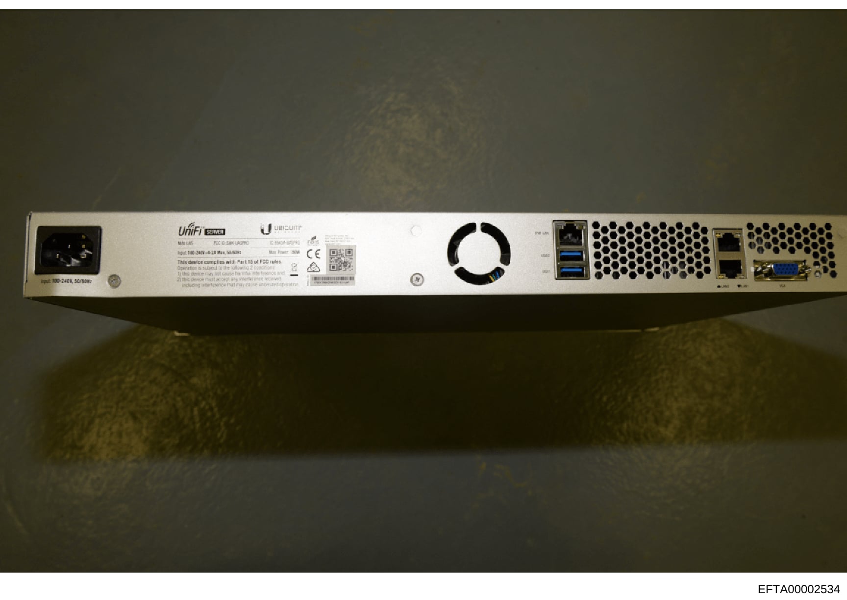 This is a photograph of the rear panel of a Ubiquiti UniFi network device, showing power connections, cooling fan, network ports, and FCC compliance information. The device appears to be server or networking equipment seized as evidence in the invest