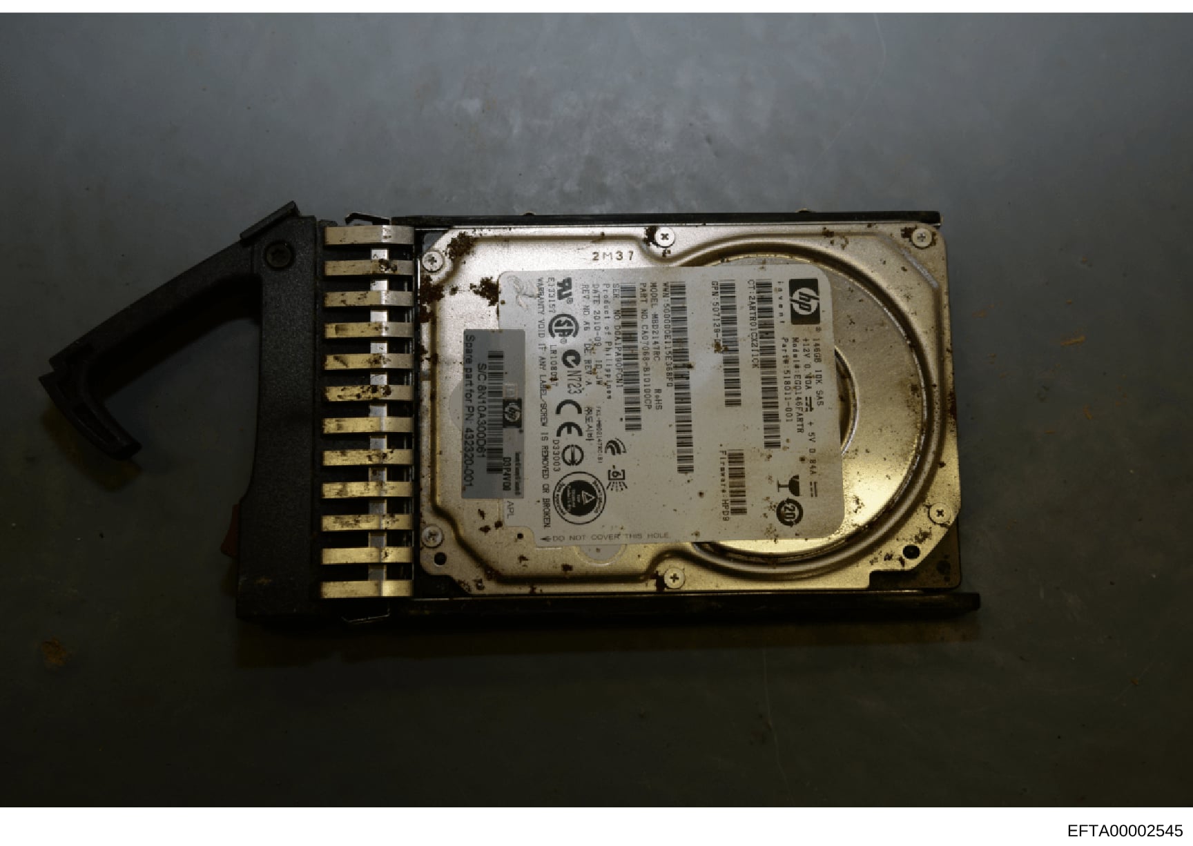 This is a forensic evidence photograph of a computer hard drive with an attached connector bracket. The drive bears visible serial numbers and identification markings, suggesting it was seized as physical evidence. The label includes HP/Compaq brandi