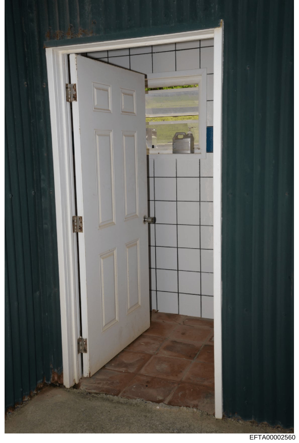 This is an evidence photograph showing the interior of a room or building space, featuring a white six-panel door, white framed doorway, and a wall with black-gridded white tiles. The image appears to be documentation of a property or location releva