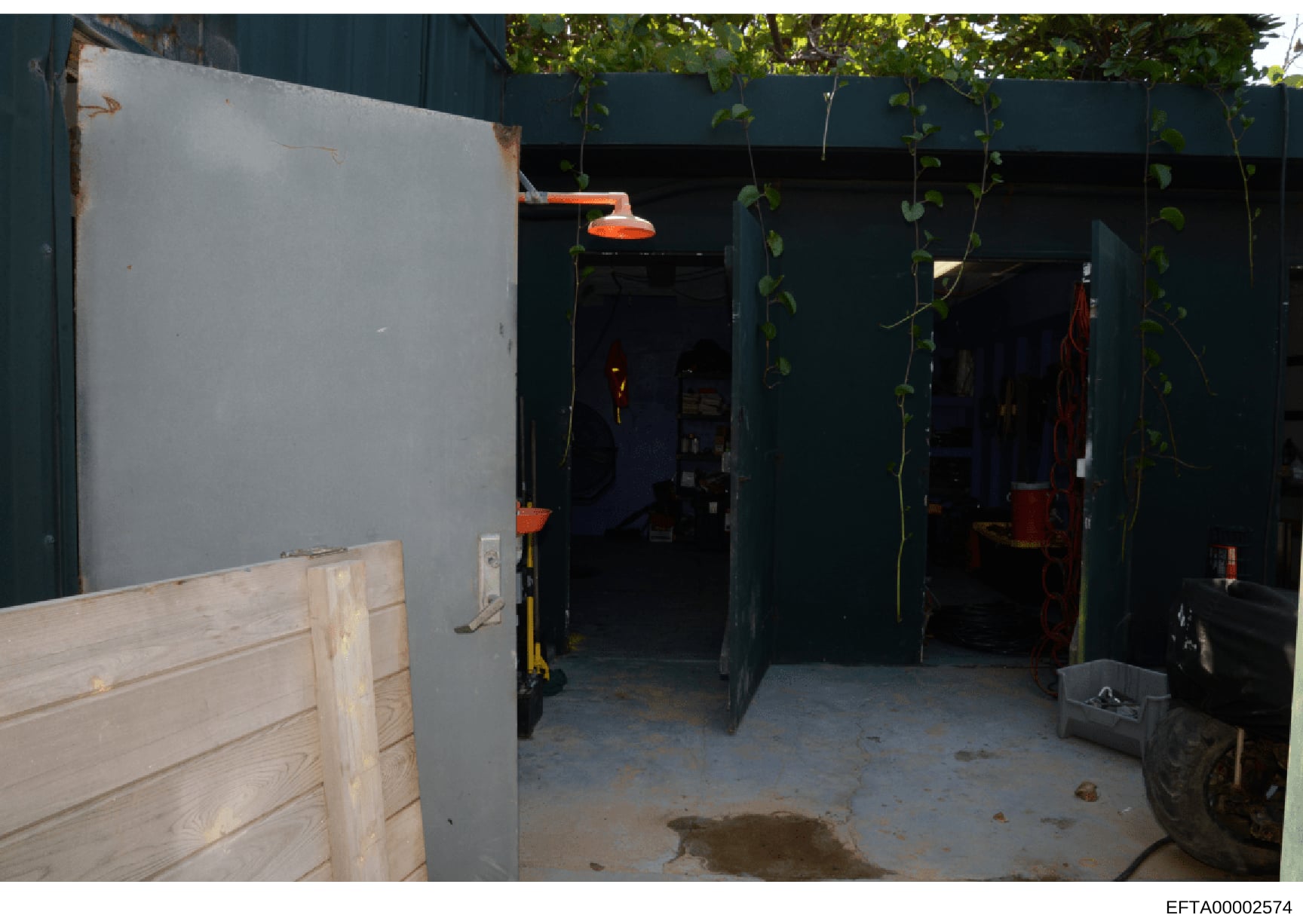 This photograph shows the interior of a large garage or storage facility with dark teal/blue painted walls, concrete flooring, and various equipment including orange-handled tools, a yellow dolly or cart, and what appears to be vehicles or large item