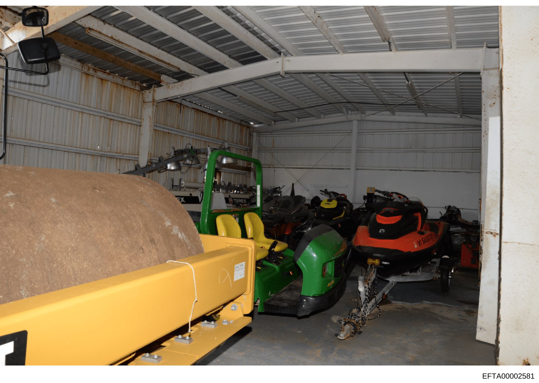 This photograph shows the interior of a large metal warehouse or storage facility containing various industrial equipment including a green and yellow forklift (Terex brand), multiple all-terrain vehicles or small utility vehicles in different colors