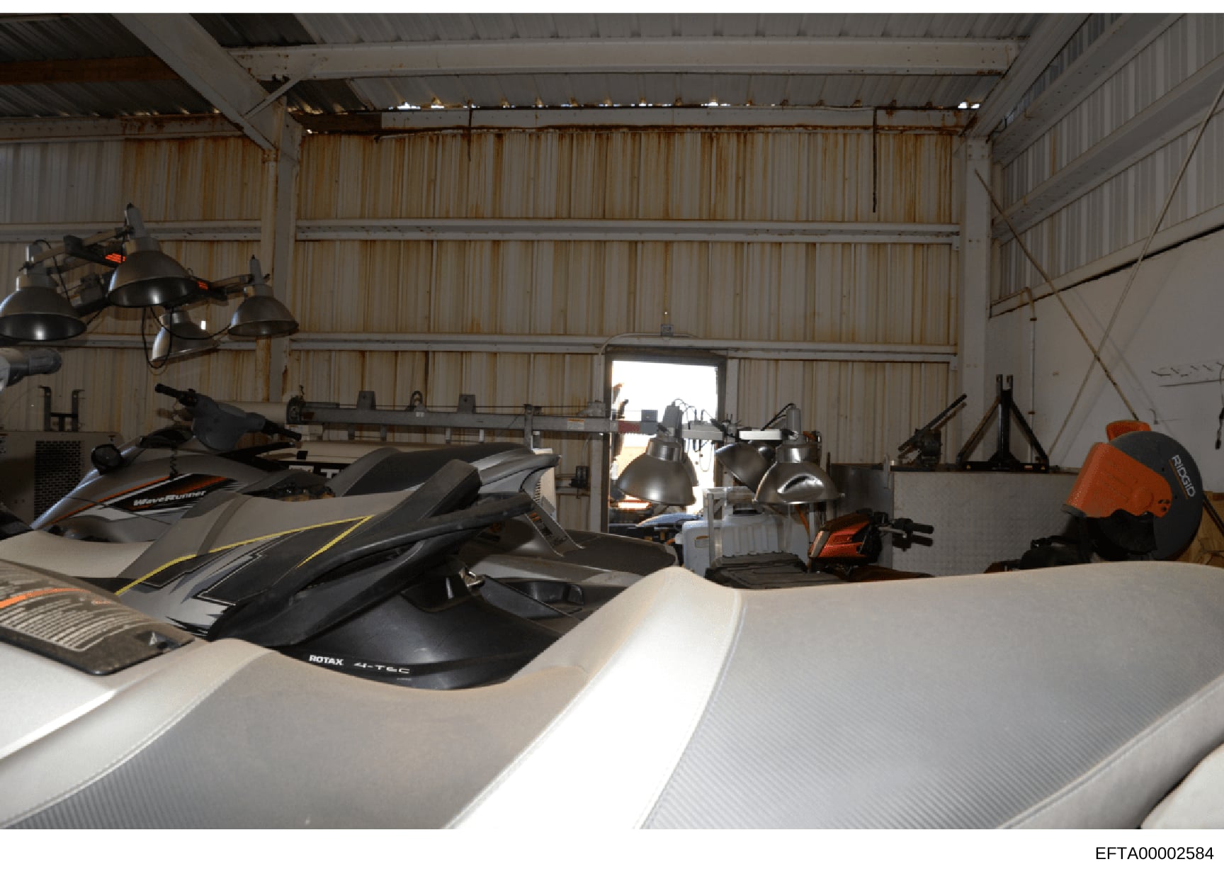 This is a photograph of the interior of a large corrugated metal warehouse or hangar containing multiple jet skis (personal watercraft), storage equipment, and industrial lighting. The space appears to be a recreational facility or storage hangar, wi