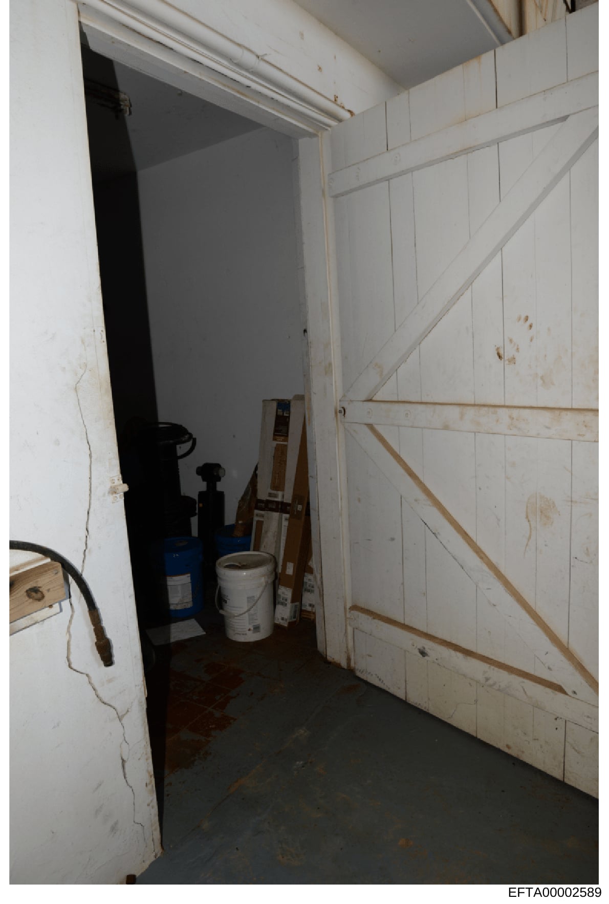 This photograph depicts the interior of a storage or utility room, showing white paneled walls, various equipment including what appears to be a blue container and white bucket, and evidence of wear and staining. The image was taken as part of the in