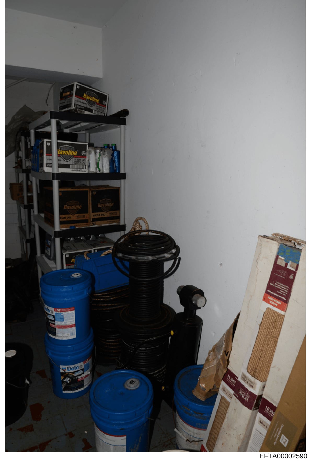 This photograph shows a residential or commercial storage area containing multiple blue drums (likely motor oil or similar automotive fluids), black storage containers, and various maintenance supplies arranged on metal shelving. The image appears to