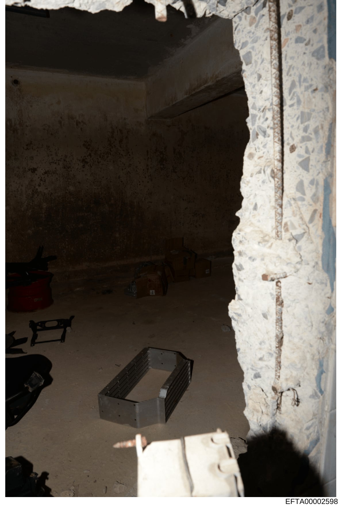 This is an evidence photograph showing an interior room in what appears to be an unfinished or under-renovation state. The image captures a concrete floor, white stone or aggregate wall finish on the right side, dark walls and ceiling, and various co