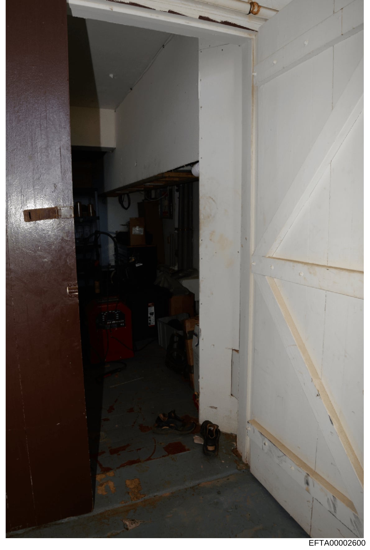 This photograph shows the interior of a room or space featuring an open doorway with a dark red/burgundy door frame on the left. Inside the doorway is visible utility equipment including what appears to be a red device or heater, drywall panels on th