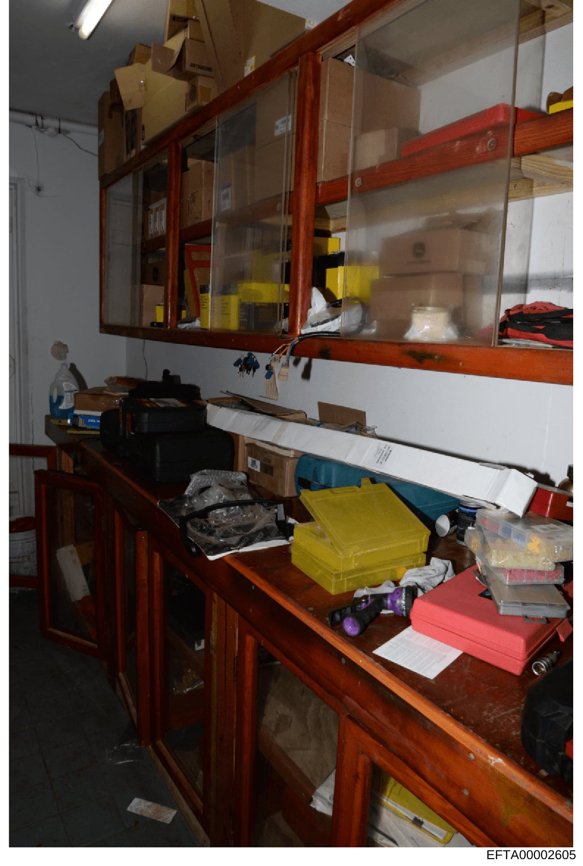This is an evidence photograph showing an interior storage room with wooden shelving units containing various boxes, containers, and materials. The image captures organized storage with labeled items in yellow and red containers, sealed boxes on shel