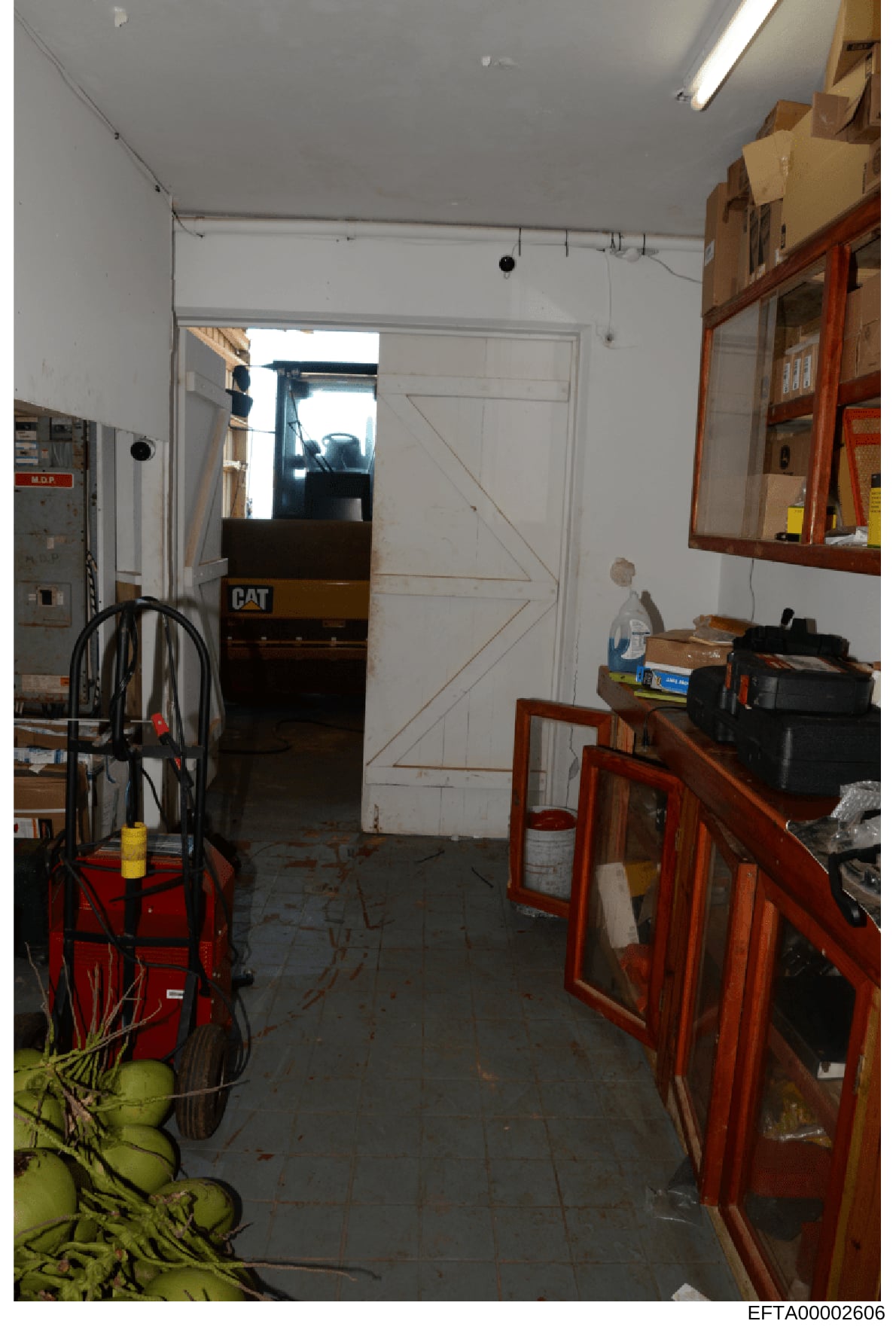 This is an evidence photograph showing the interior of a storage area or garage space, likely taken during an investigation. The space contains various tools, equipment, and household items including a red mechanical device on the left, wooden cabine