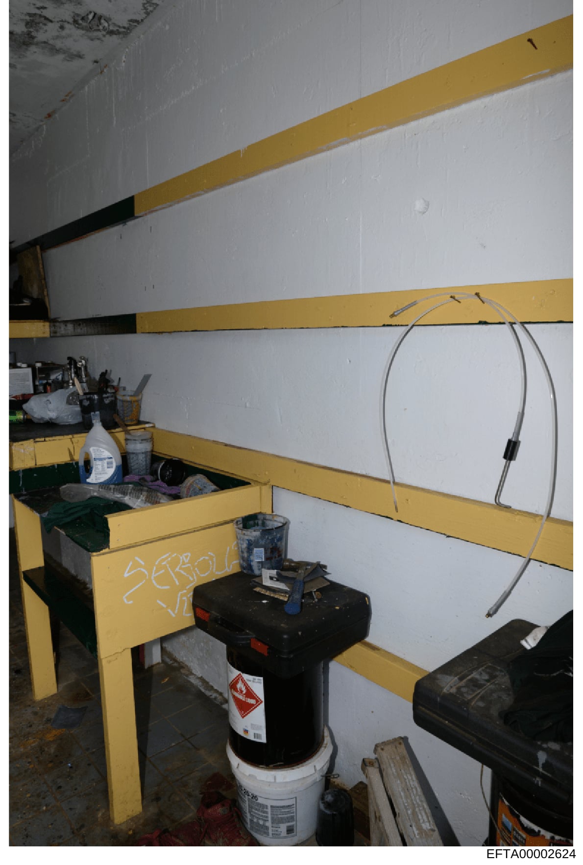 This is a photograph of an interior storage or utility room, likely from one of Epstein's properties, showing yellow metal shelving units with white walls and various stored items including containers, cables, and equipment. The space appears to be a