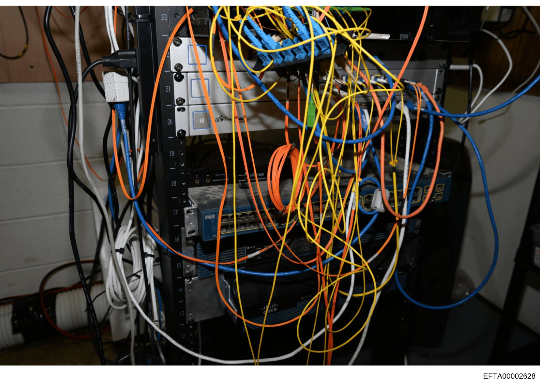 This photograph shows a close-up view of electrical or networking equipment with multiple colored cables (orange, yellow, blue, black, and white) connected throughout. The image appears to be documentation of technical infrastructure, possibly from a