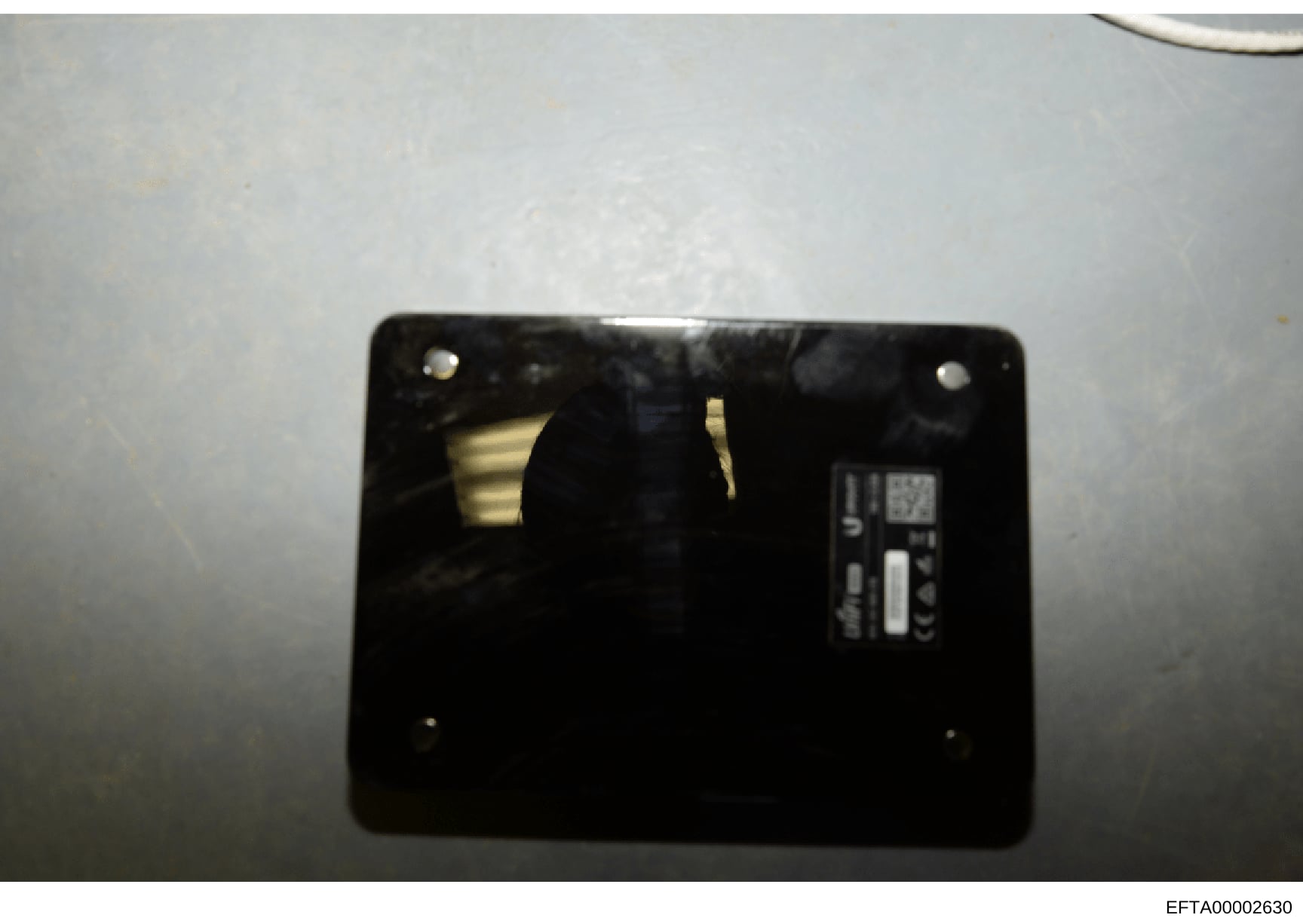 This is a close-up forensic photograph of the interior of an electronic device, showing a black circuit board or component panel with mounting points and what appears to be a manufacturer label or serial number plate on the right side. The image qual