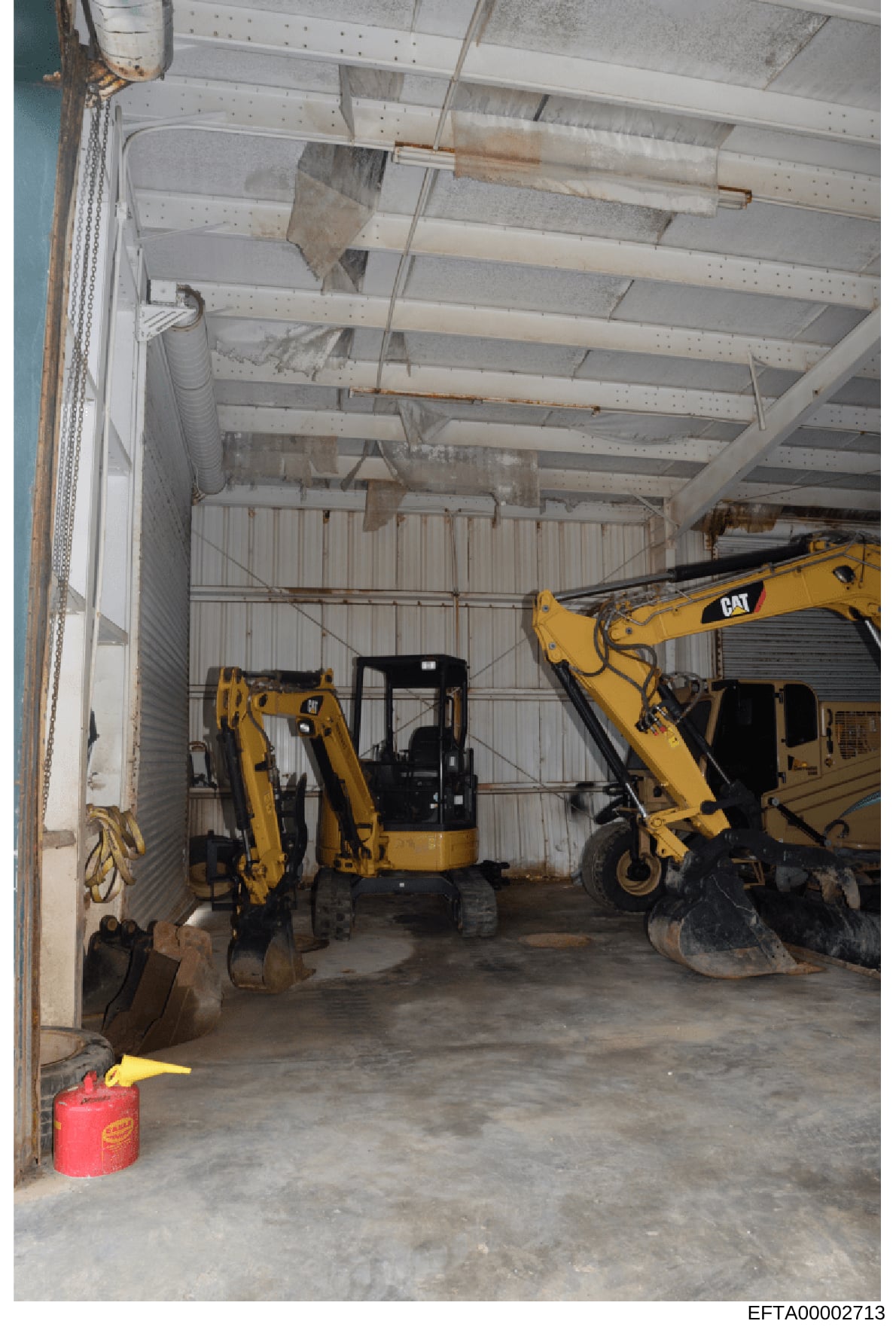 This photograph shows the interior of an industrial or construction equipment storage facility containing multiple CAT (Caterpillar) brand excavators and heavy machinery. The image documents the physical condition and contents of what appears to be a