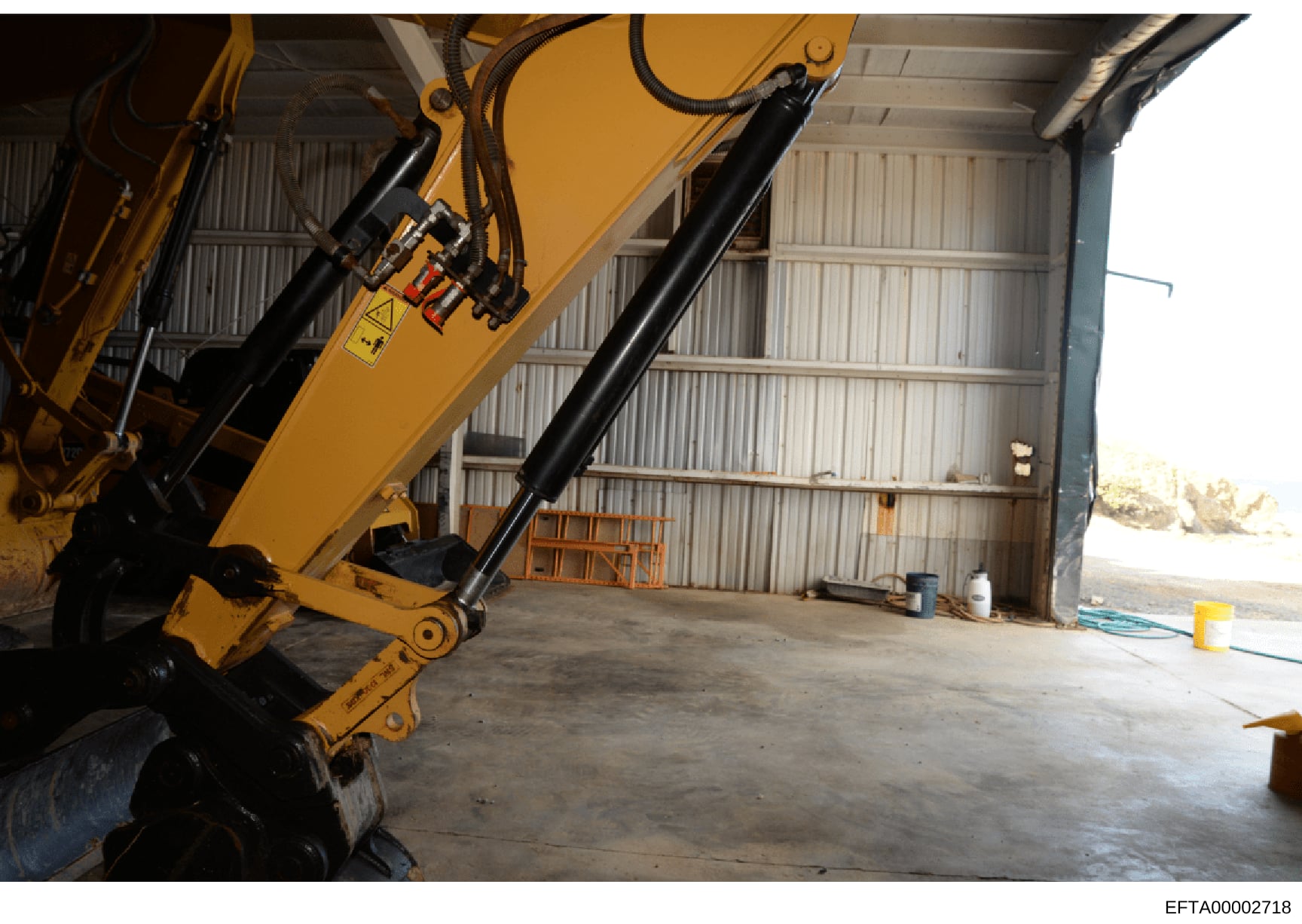 This photograph shows the interior of an industrial warehouse or storage facility containing large yellow hydraulic equipment, likely a crane or material handling machine. The image appears to be documentary evidence capturing the physical space and