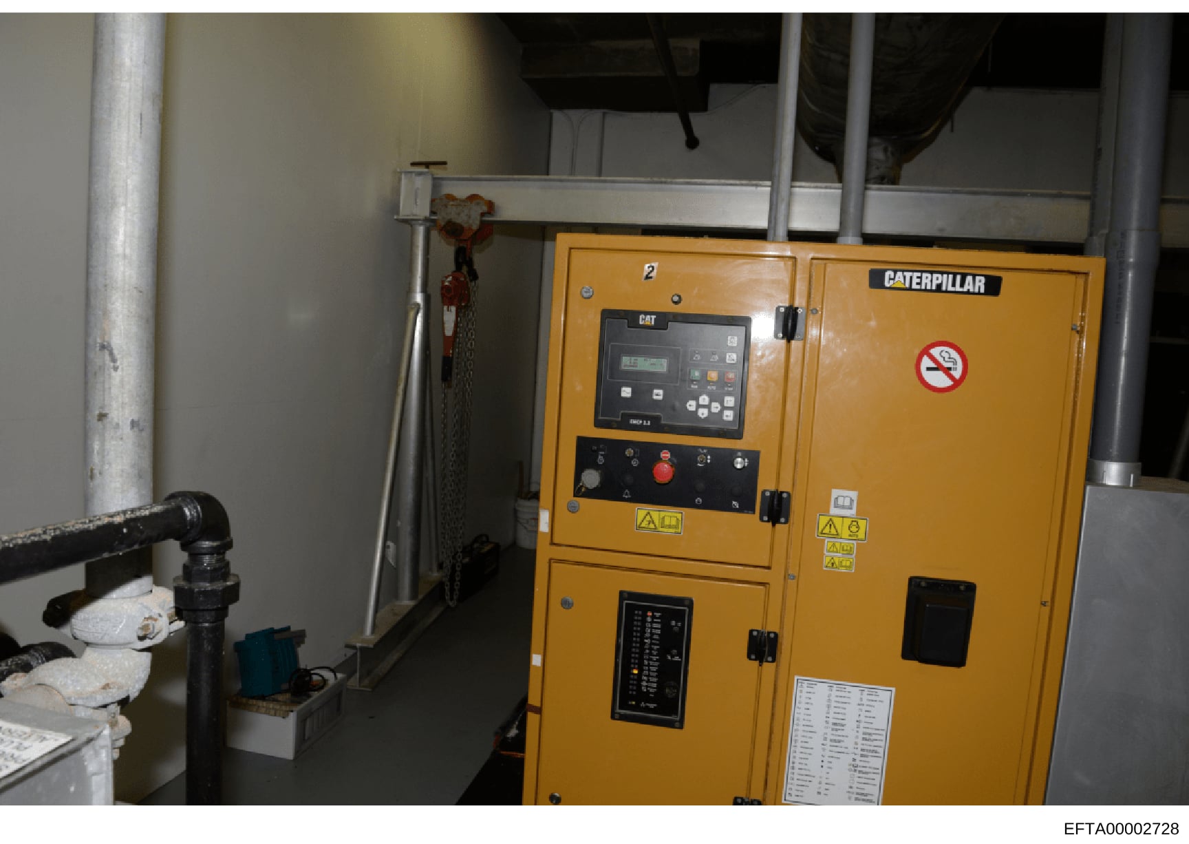 This photograph shows a large yellow Caterpillar diesel generator unit installed in what appears to be a building's mechanical or utility room. The generator features control panels, electrical switches, and safety warnings. The image is relevant as