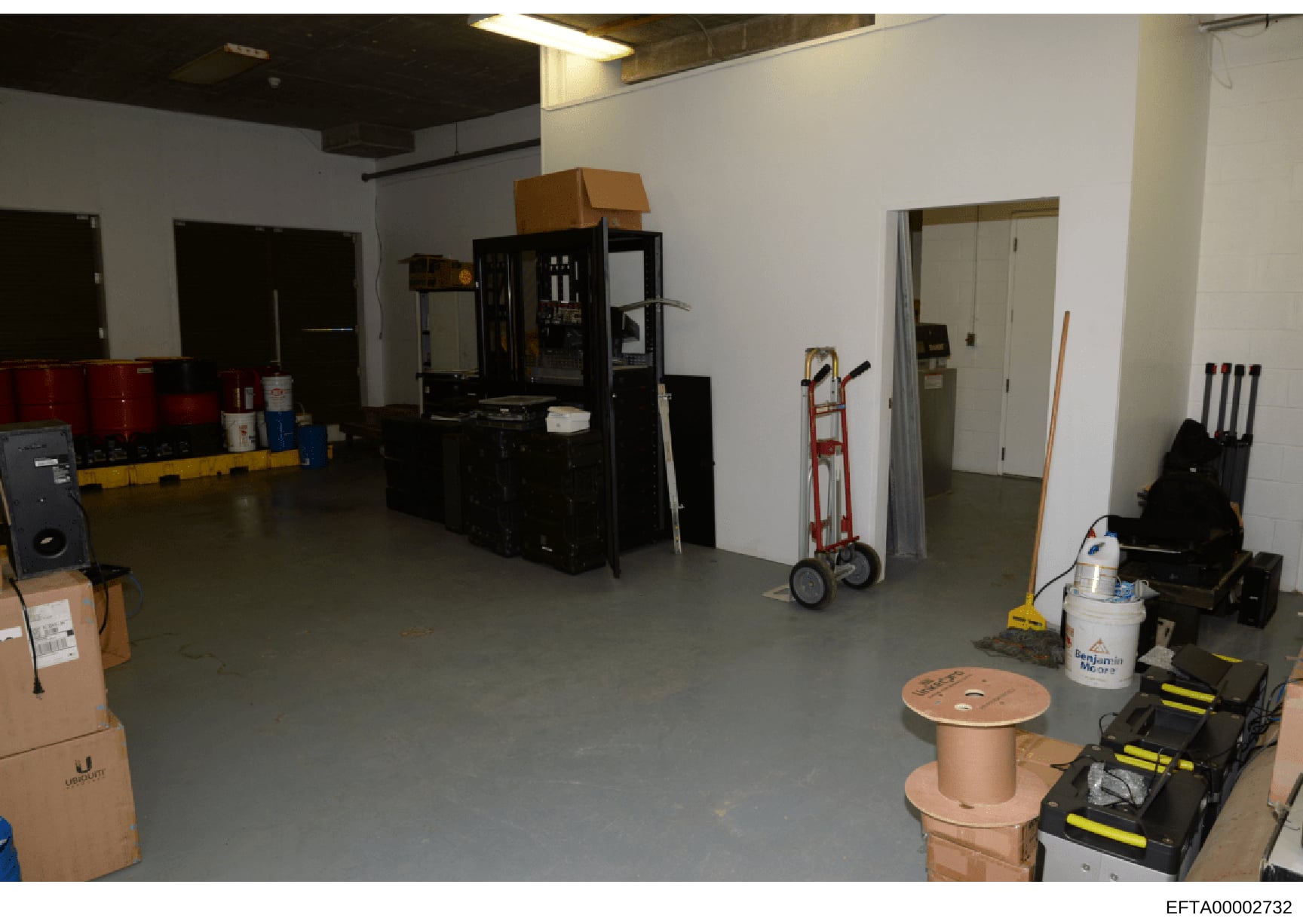 This is a photograph of an interior industrial or warehouse space showing various equipment, machinery, and storage items. The space appears to be under renovation or preparation, with exposed ceiling elements, cardboard boxes, industrial machinery (