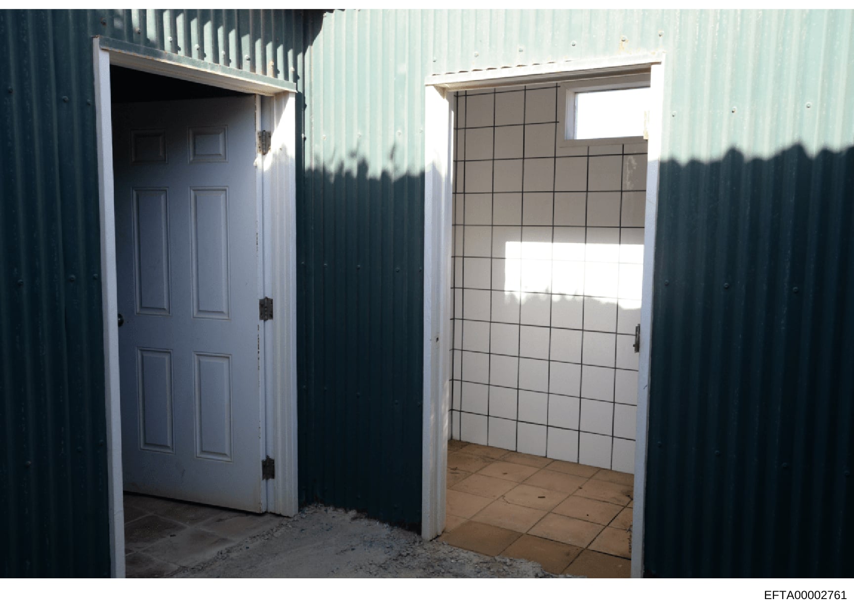This photograph shows the exterior and interior entrance of a metal-sided structure, featuring a white six-panel door on the left and a tiled interior room visible through an open doorway on the right. The image appears to be evidence documentation f