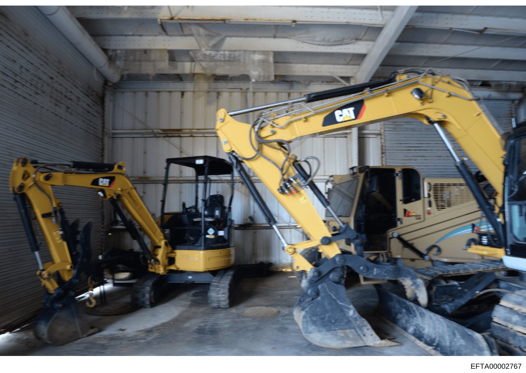 This is a photograph of an industrial warehouse or storage facility containing multiple pieces of heavy construction equipment, primarily yellow Caterpillar (CAT) excavators. The image shows at least three excavators of varying sizes stored in a meta