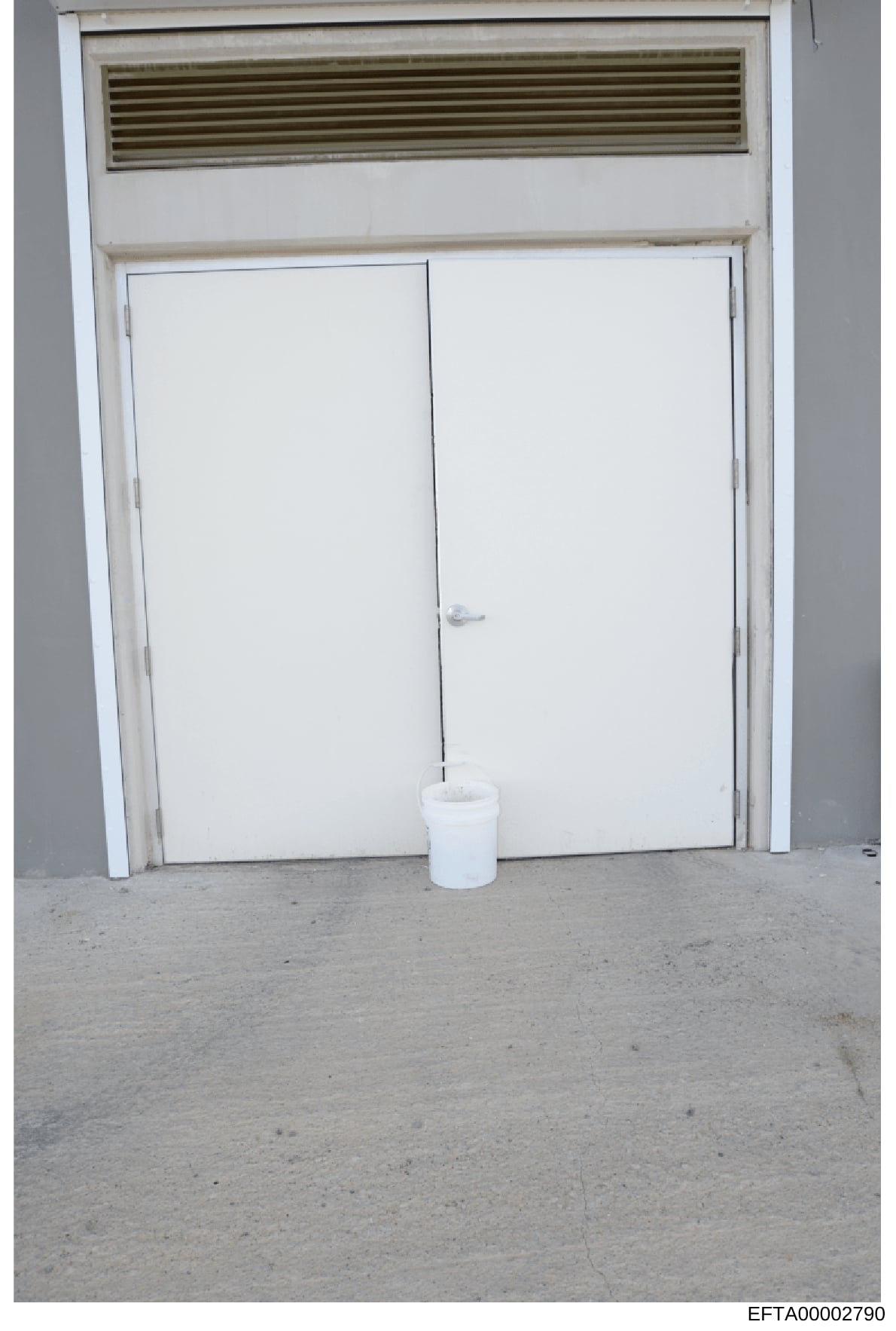 This is an evidence photograph showing the interior of a property, depicting a double white door with an overhead ventilation/air return system and a white bucket on the floor. The image appears to be part of property documentation or evidence collec