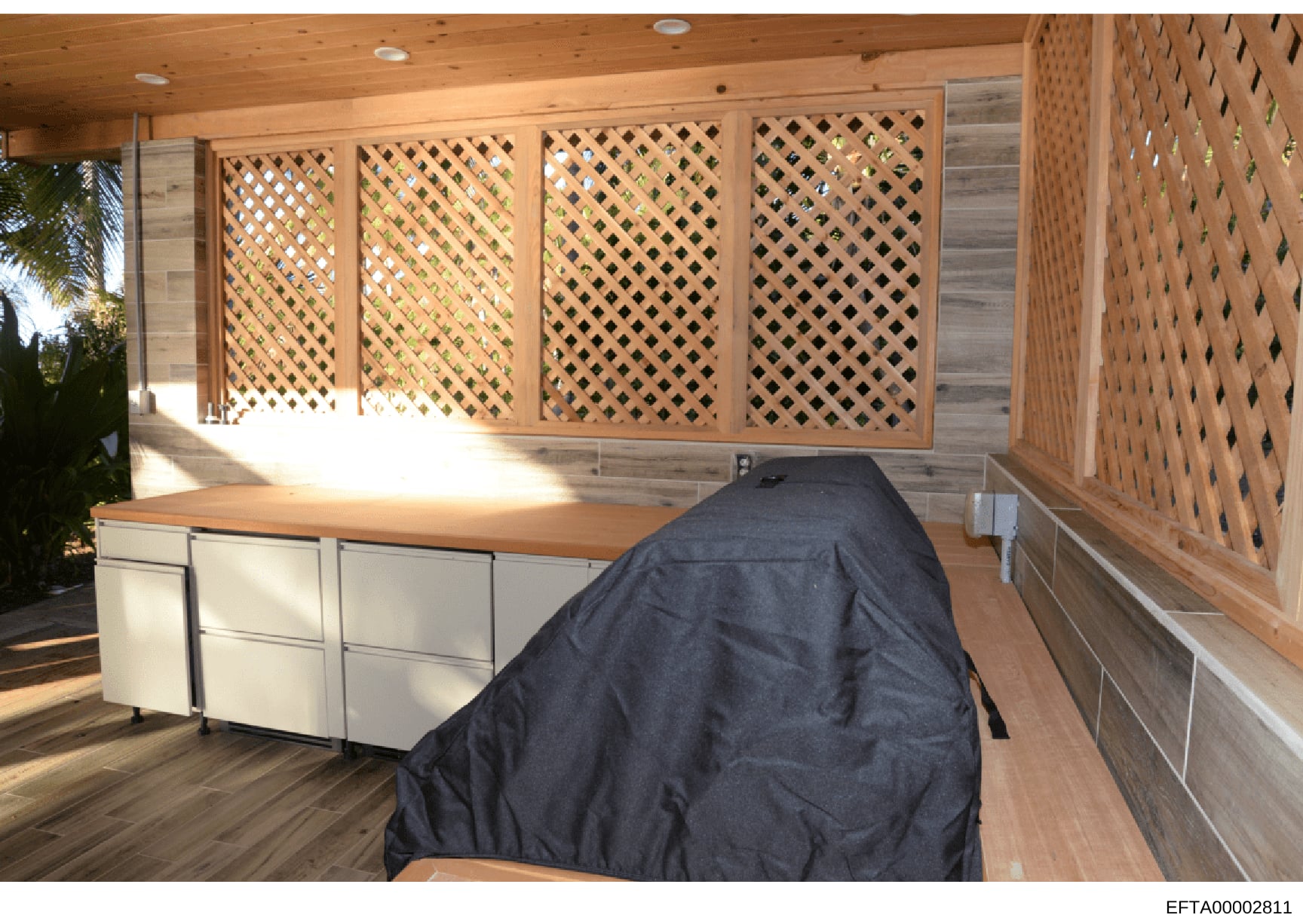 This is a photograph of an outdoor covered structure featuring lattice paneling, wooden construction, and built-in cabinetry. The image shows a modern pavilion or gazebo with decorative diamond-pattern lattice screens on multiple walls, white cabinet