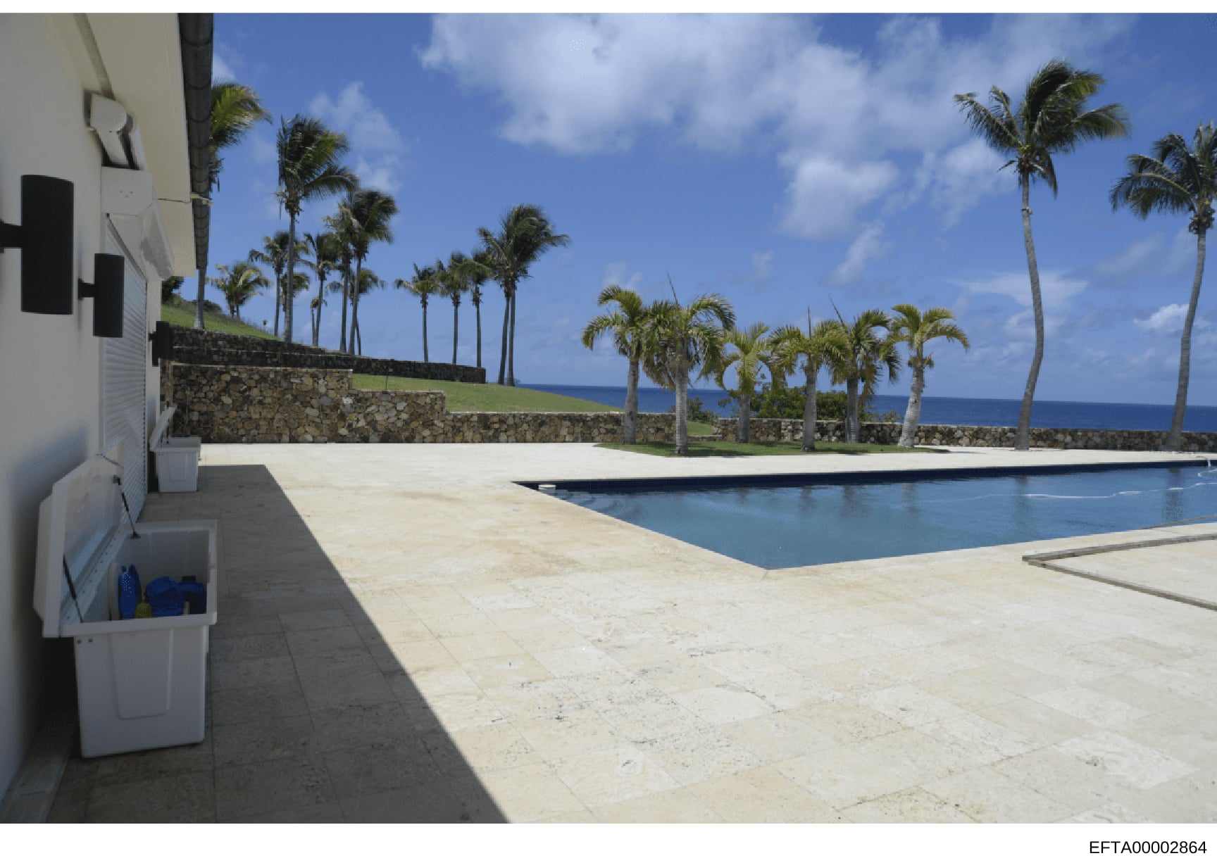This photograph shows the exterior of a luxury oceanfront property featuring a swimming pool, expansive patio deck, manicured grounds with palm trees, and ocean views. The image appears to be documentation of a residential property likely owned or as
