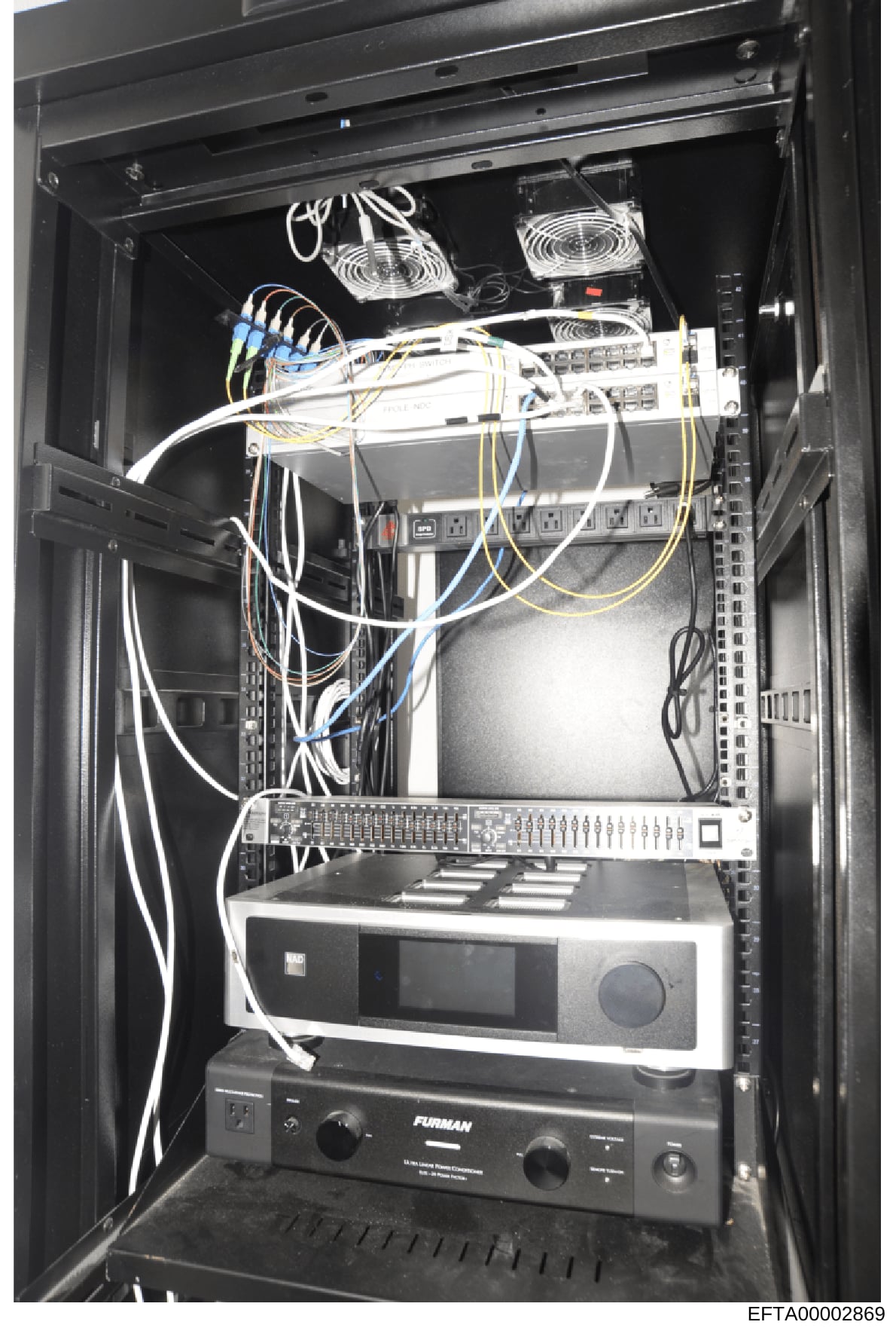 This is a photograph of a professional server rack containing networking and audio/visual equipment. The image shows multiple devices including cooling fans, network switches, amplifiers, and cabling infrastructure. This type of equipment documentati