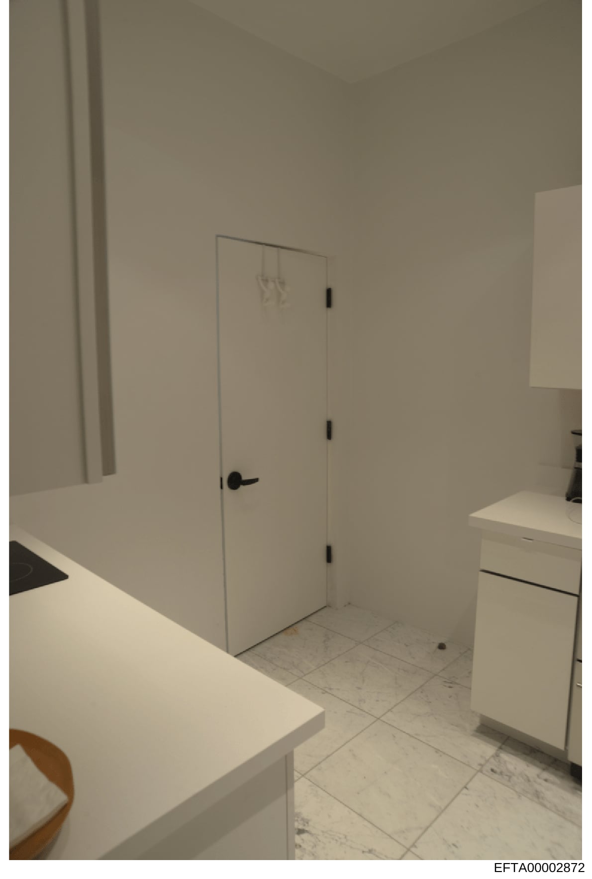 This is an evidence photograph showing the interior of a room with white walls, tile flooring, a closet with a black handle and hinges, and what appears to be bathroom or kitchen cabinetry on the right side. The image is from the Epstein investigatio