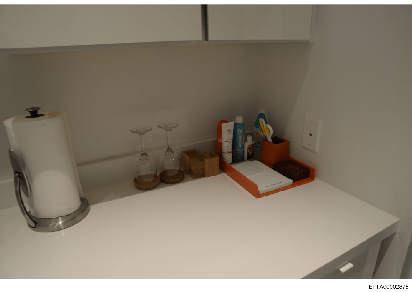 This is a photograph of a kitchen counter or shelf space showing various household items including a paper towel holder, glassware, decorative containers, and personal care products. The image appears to be an evidence photo from a property search or