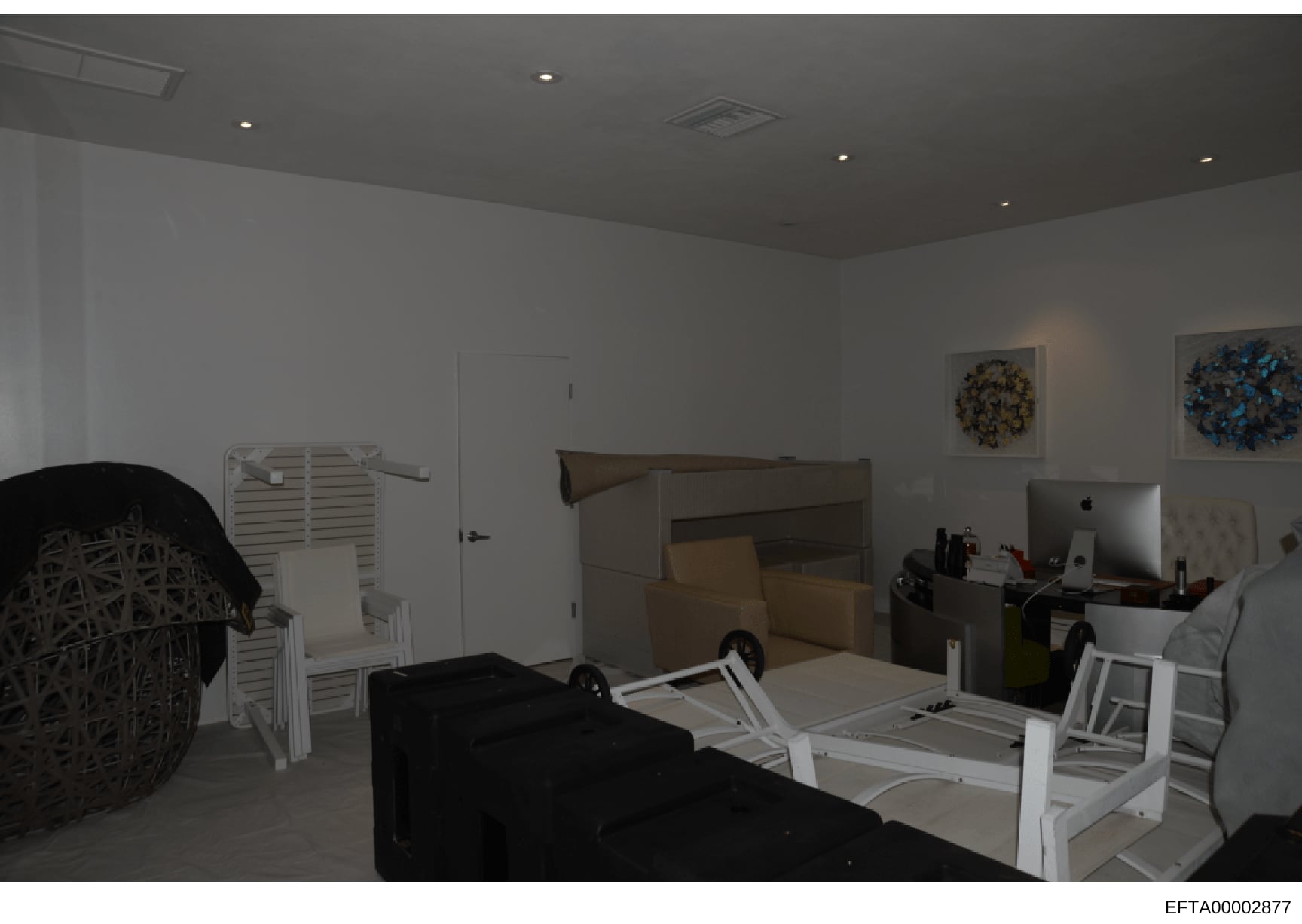 This is a photograph of an interior room, likely a bedroom or office space, showing various furniture items including a bed frame, desk with computer equipment, white storage units, and decorative wall art. The image appears to be evidence documentat