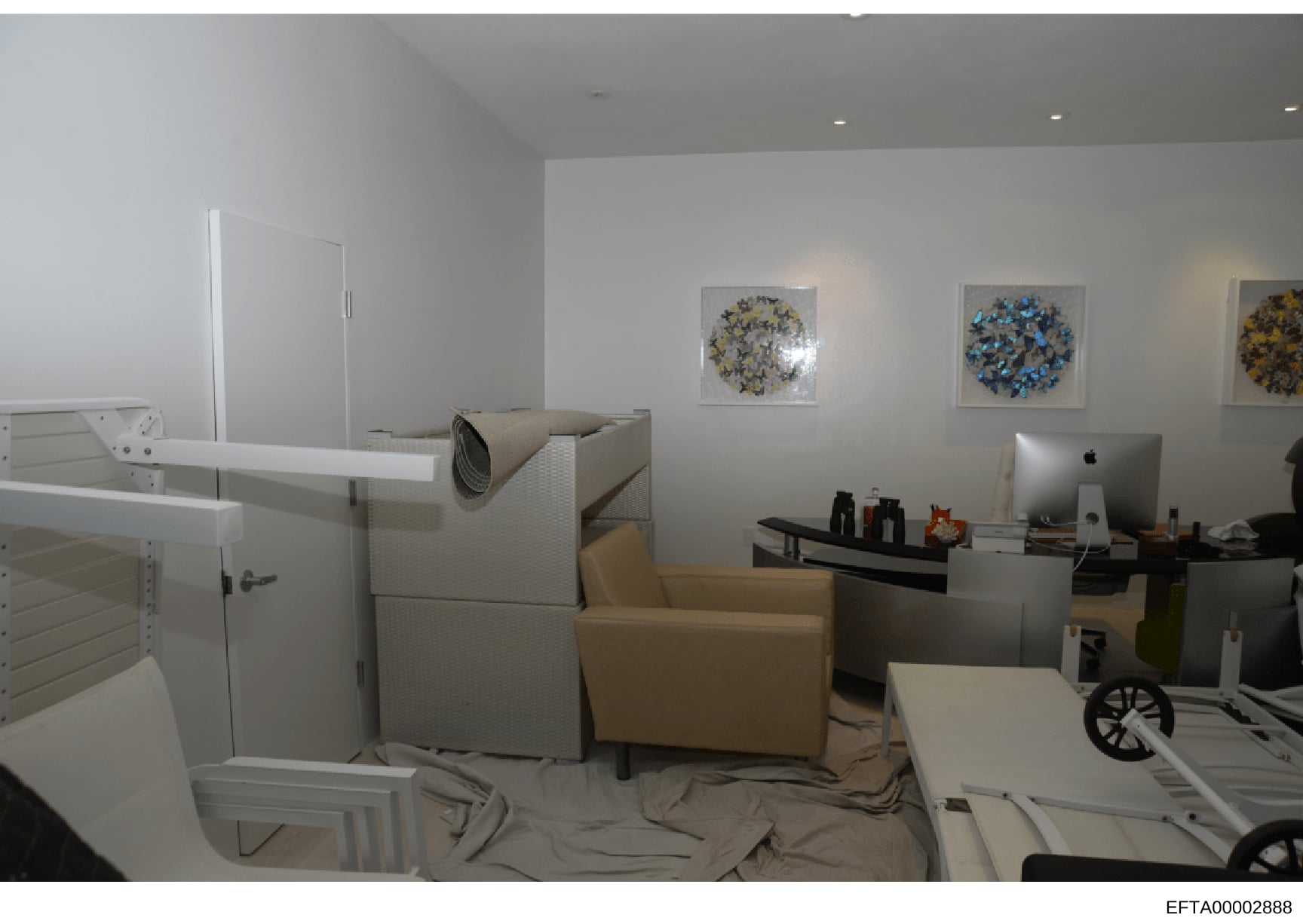 This photograph depicts an interior room with modern furnishings and decor, including a tan/beige armchair, white cabinetry, a desk setup with computer monitor, and wall art featuring circular blue and yellow designs. The room appears to be a residen