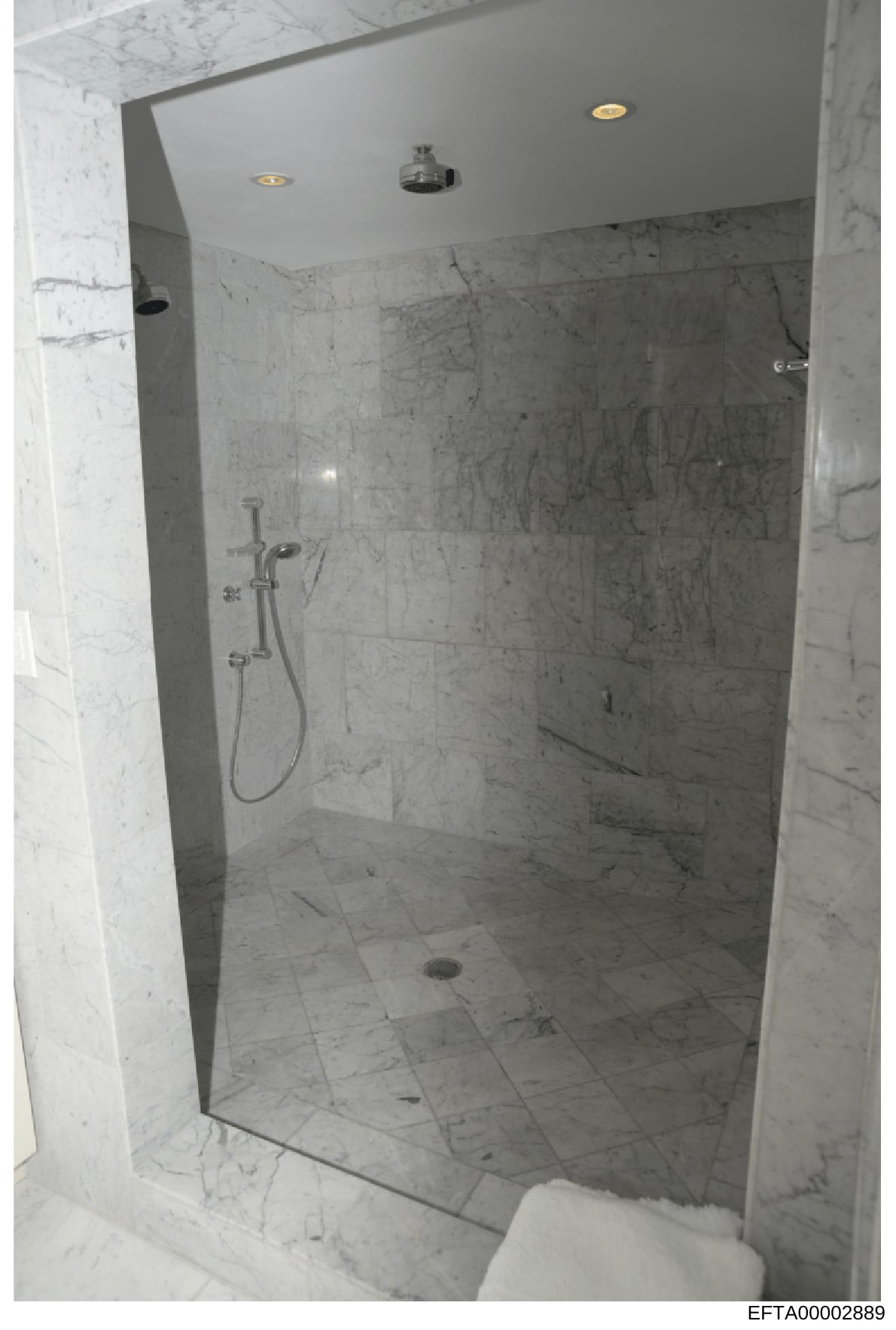 This is a photograph of a modern, upscale bathroom shower enclosure with marble tile walls and floor. The image appears to be an evidence or property documentation photo taken as part of the investigation, showing the interior finishes and fixtures o