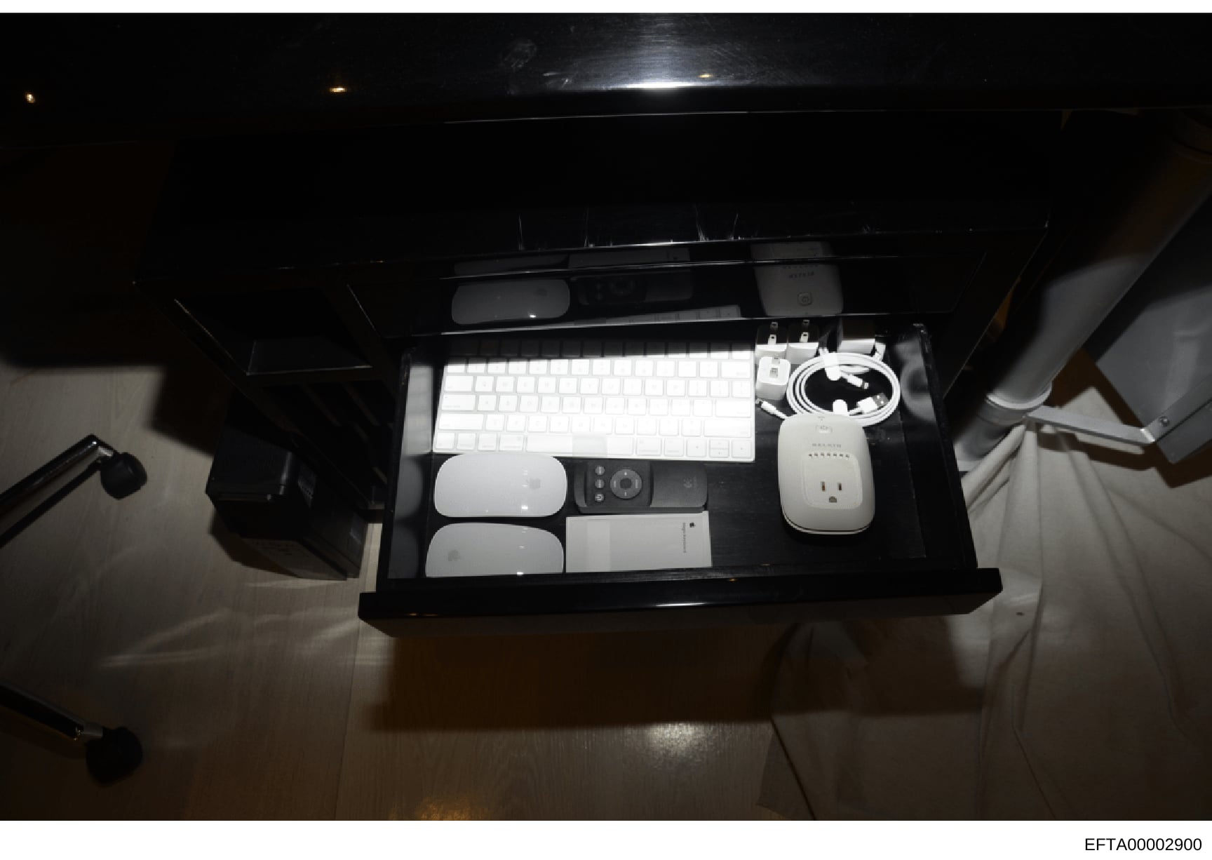 This is an evidence photograph showing a black desk organizer containing computer equipment including a white keyboard, mouse, remote control, power adapter, cables, and other electronic accessories. The photo appears to be part of a physical evidenc