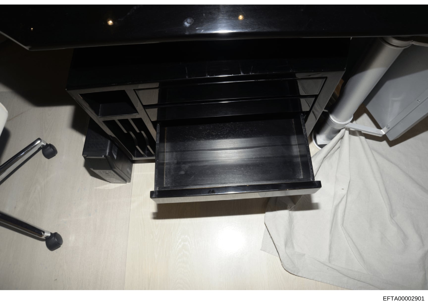 This is an overhead photograph showing a black furniture item, possibly a desk, shelf unit, or cabinet, positioned in an interior room with light-colored flooring and white walls. The image appears to be evidence documentation from a property search