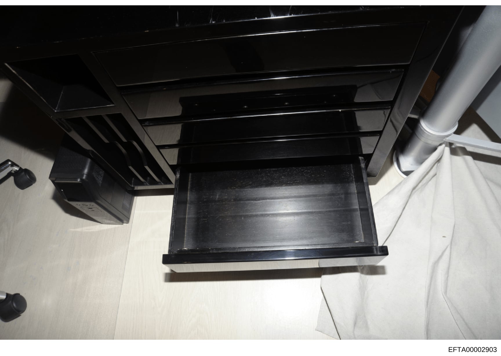 This is an evidence photograph showing a black wooden furniture item, likely a desk or cabinet, with an open drawer. The image appears to be taken from above at an angle, showing the interior construction and hardware. The photograph includes visible