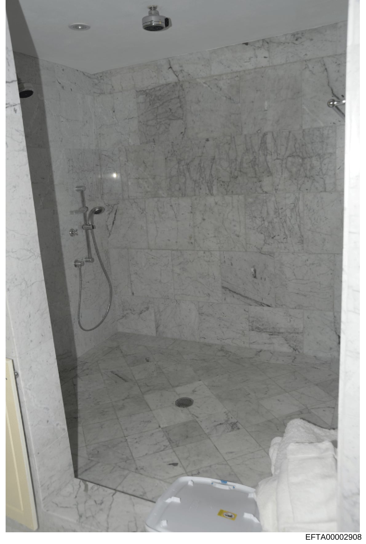 This is an evidence photograph documenting the interior of a luxury bathroom featuring marble tile walls and flooring, a walk-in shower with glass enclosure, and modern fixtures. The image appears to be part of property documentation or evidence coll