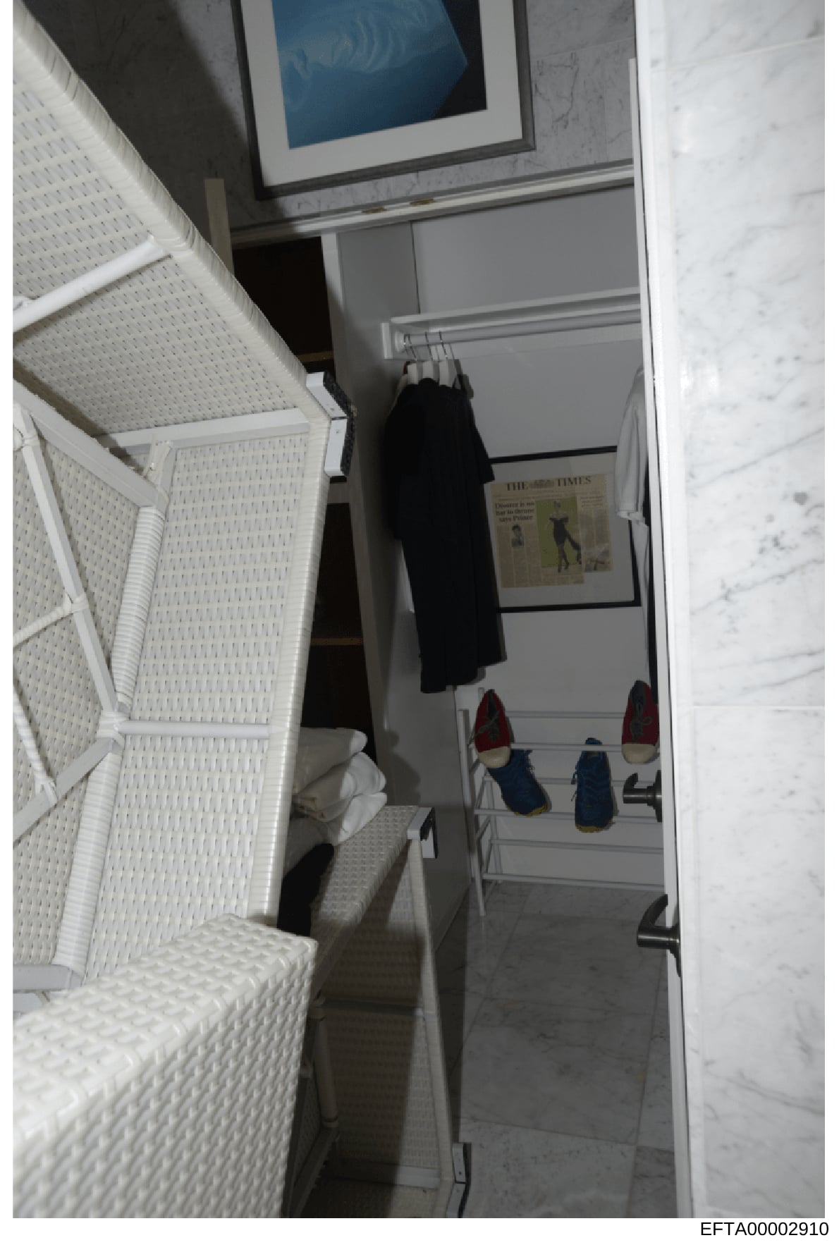 This is an evidence photograph showing the interior of a closet or small dressing room, featuring white shelving with folded linens or textiles, hanging clothing (including a black garment), footwear on lower shelves, and what appears to be a framed