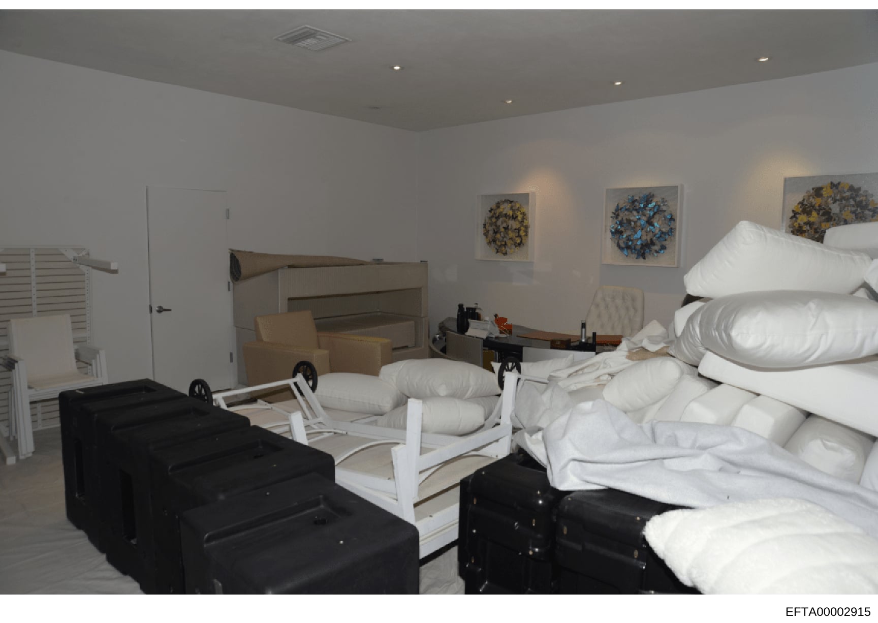 This is an evidence photograph showing the interior of a bedroom, likely from one of Jeffrey Epstein's properties. The room contains multiple beds with white bedding, black storage chests, decorative artwork on the walls, and various furnishings. The