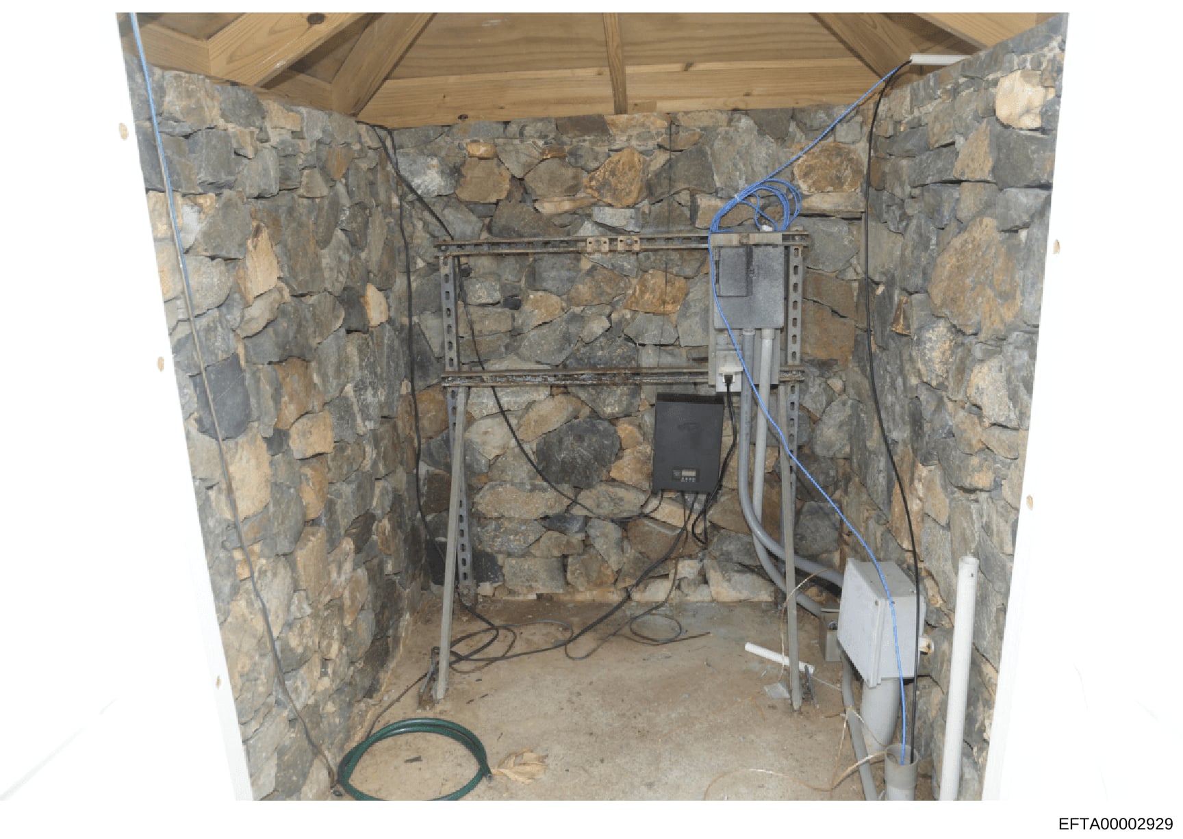 This photograph shows the interior of a stone-walled structure, likely a utility room, storage area, or building foundation space. The image documents electrical wiring, equipment mounting systems, and building infrastructure. The stone construction 
