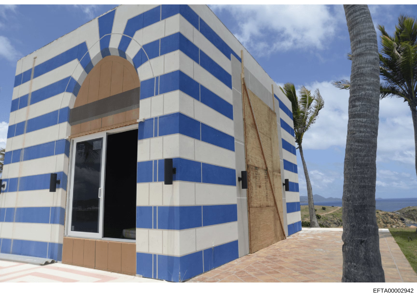 This is a photograph of a distinctive residential or commercial structure located on a coastal property. The building features a striking blue and white horizontal striped exterior with tan/brown trim and accents. The structure appears to be modern i