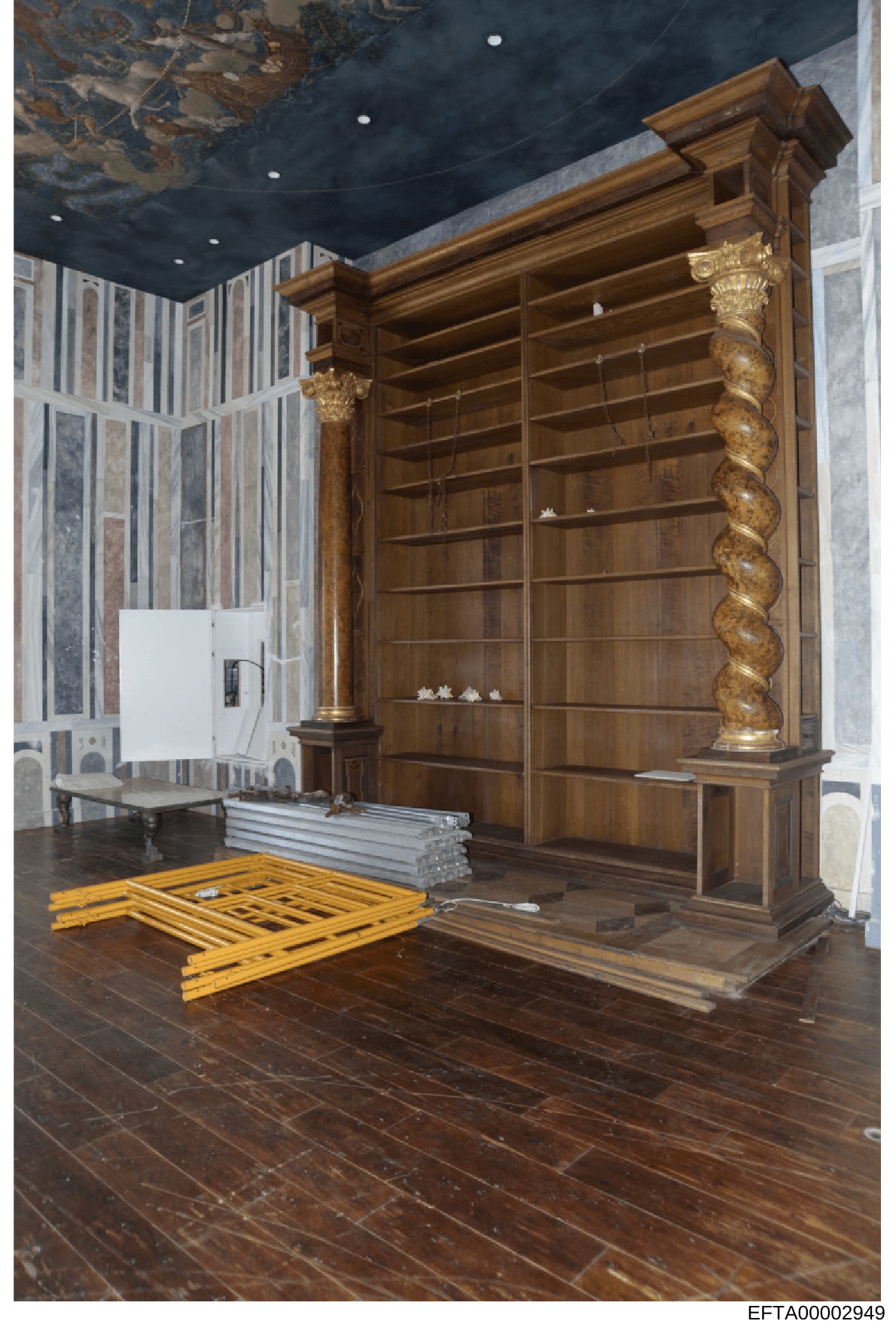 This photograph depicts an interior room with high-end architectural features, including a large custom wooden bookcase or display cabinet with ornate gold-leaf columns, decorative ceiling with dark blue finish and painted details, and marble/stone w