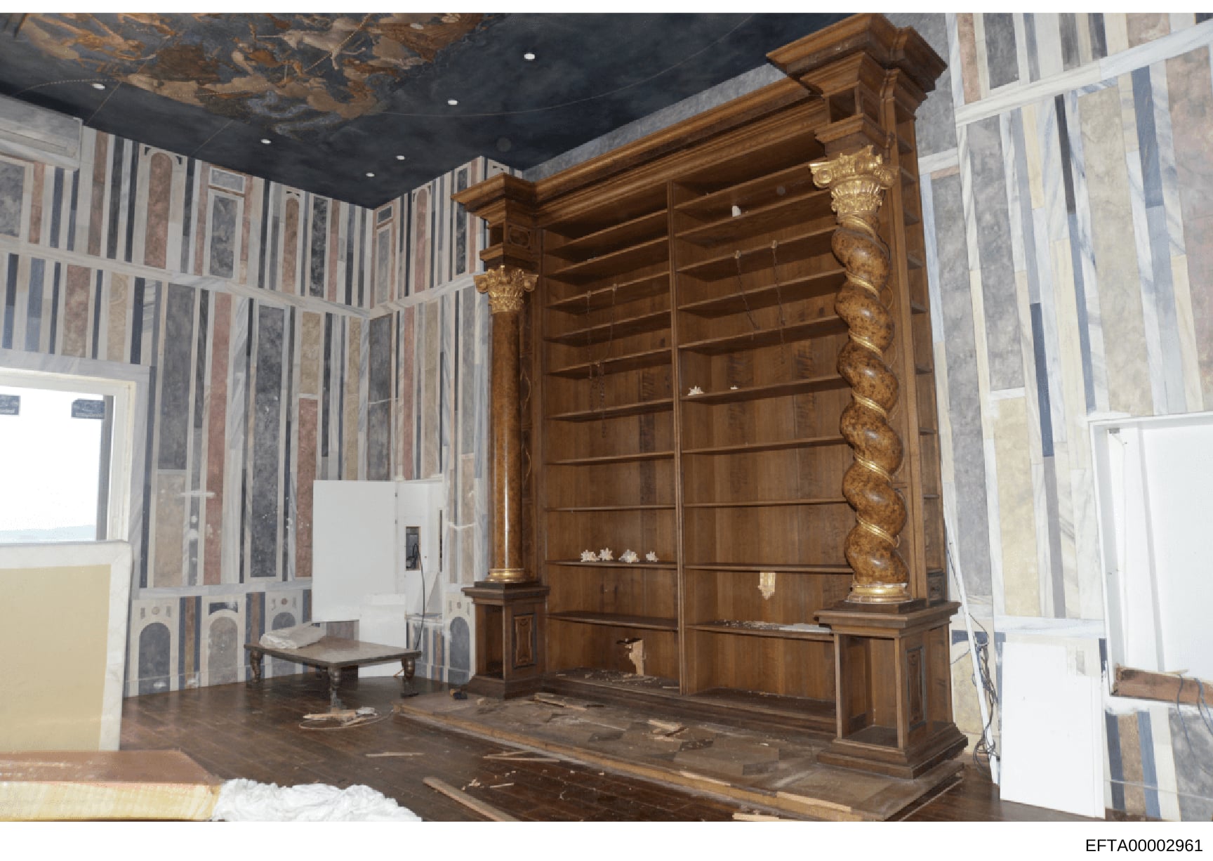This photograph shows a high-end interior space featuring an elaborate wooden built-in bookcase with ornamental columns, striped wallpaper, and decorative ceiling details. The room appears to be part of a luxury residence or estate, likely documented
