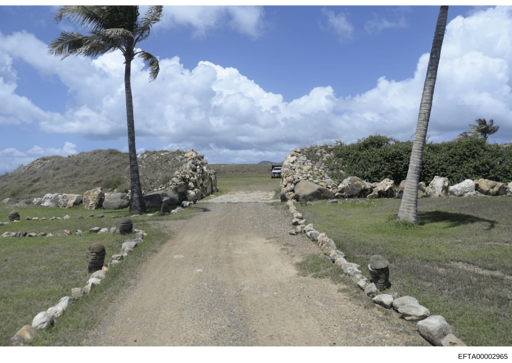 This photograph shows the entrance to a remote tropical property, marked by a distinctive stone gateway made of stacked rocks flanking a dirt driveway. The image appears to be evidence documentation of a location associated with the Epstein investiga