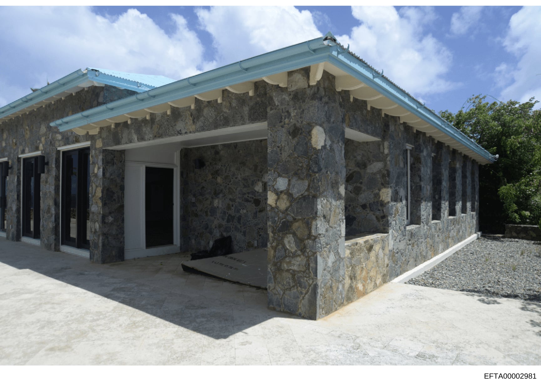 This photograph shows the exterior of a contemporary residential building featuring distinctive dark stone walls with light-colored accents, turquoise metal roofing, and modern architectural design. The structure appears to be a property potentially