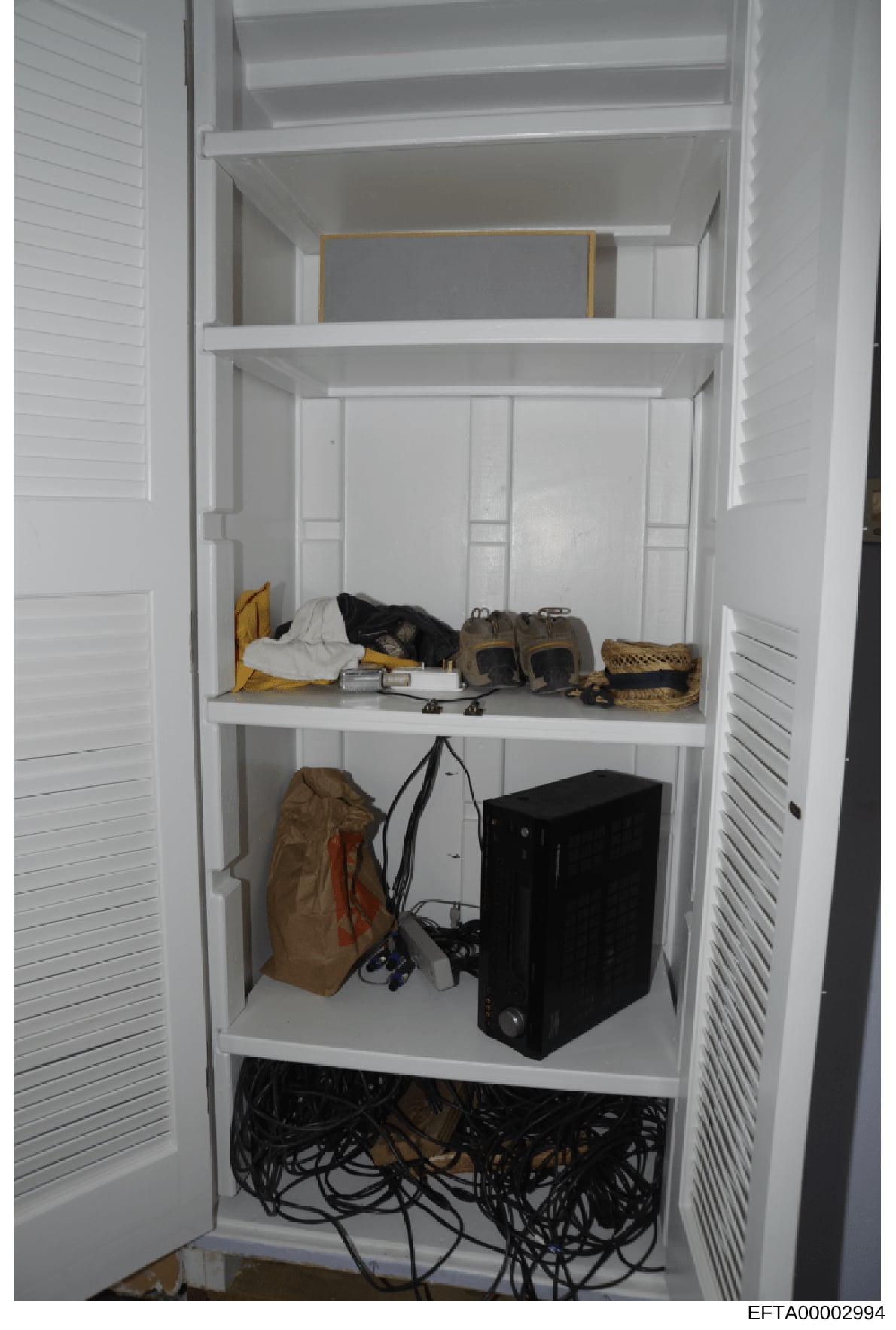 This photograph shows the interior of a white built-in closet containing various items including clothing, electronics (a black computer tower), cables, bags, and personal belongings. The image appears to be evidence documentation of property content