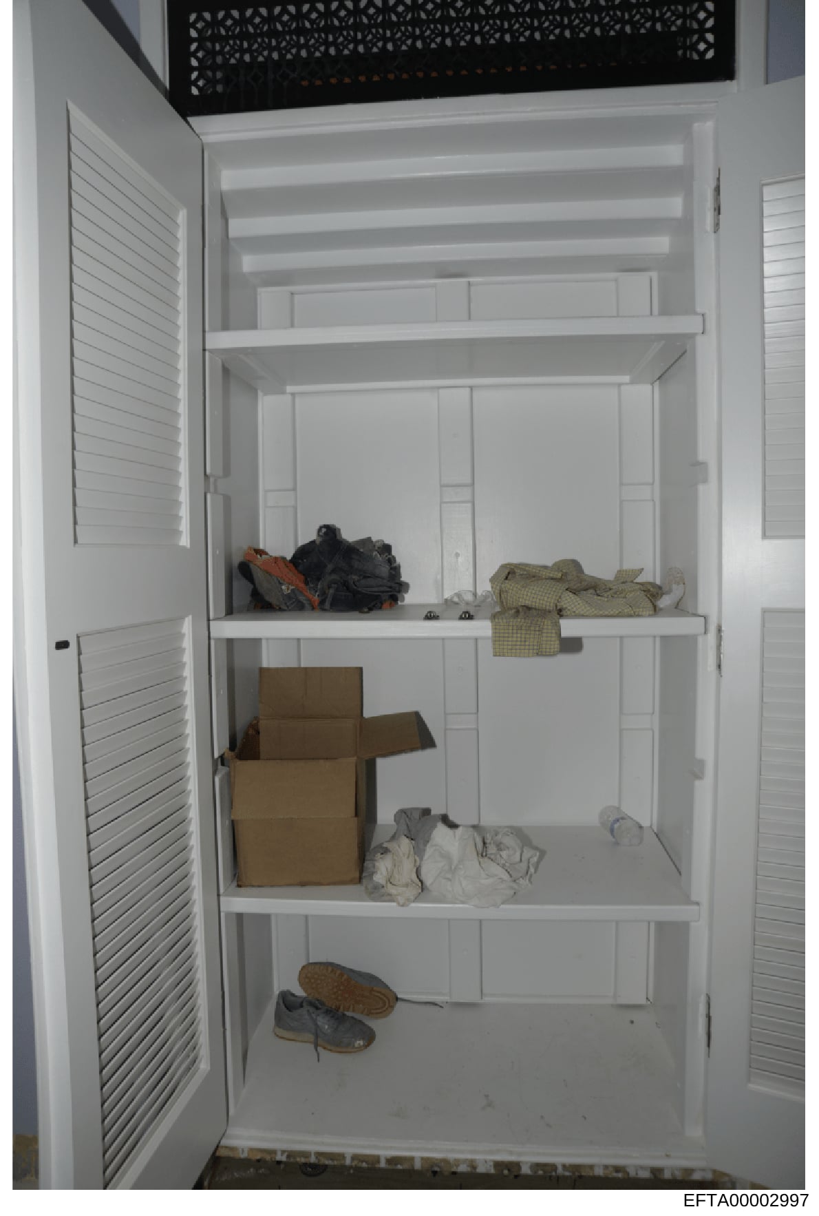 This is an evidence photograph showing the interior of a white closet or storage cabinet containing various items including clothing, boxes, and shoes. The image appears to be part of the documentary record from the Epstein investigation, likely take