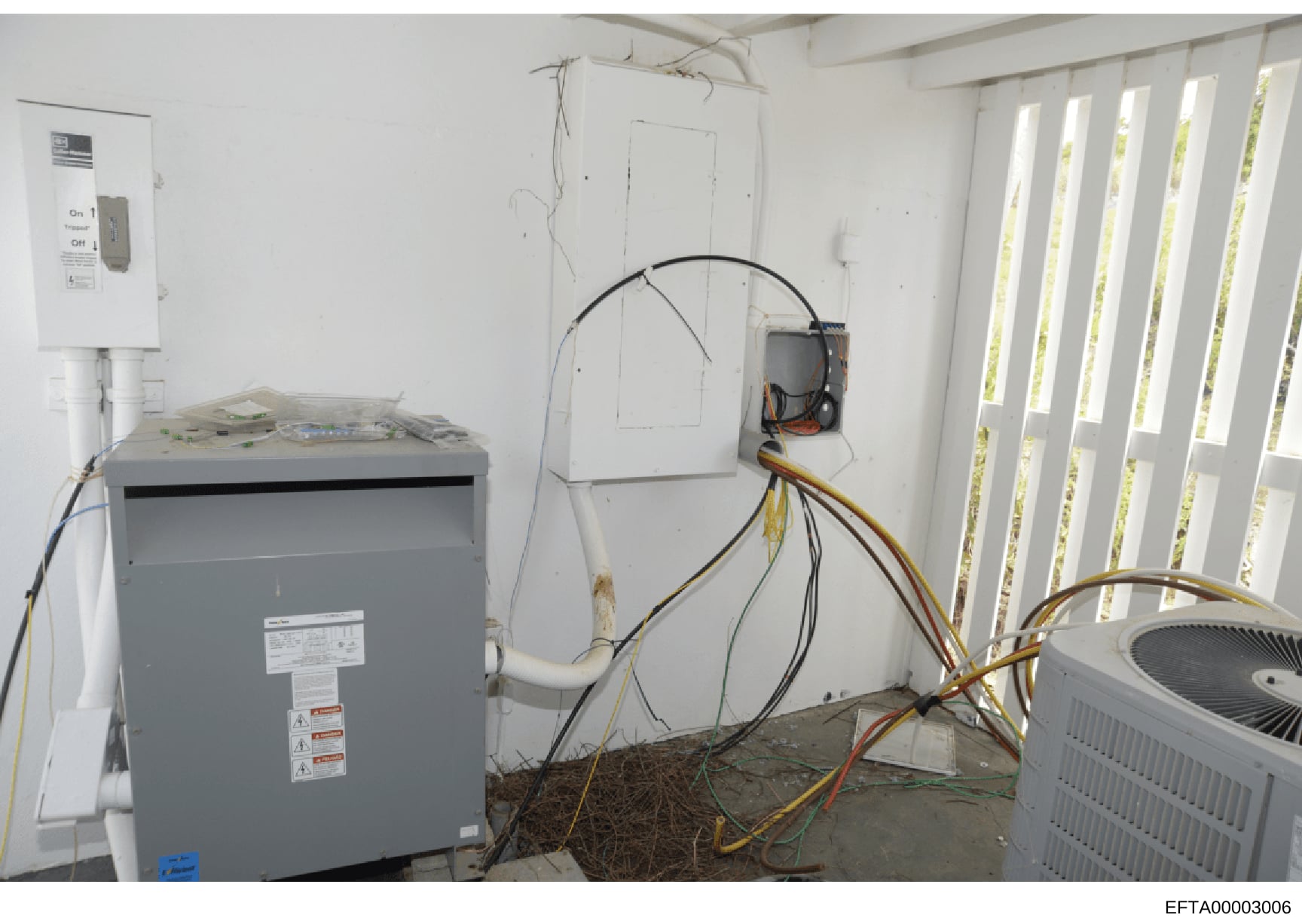 This photograph shows an HVAC system installation in progress within a property, featuring a gray transformer/electrical box on the left, exposed wiring, electrical panels, and air conditioning units. The image documents the mechanical and electrical