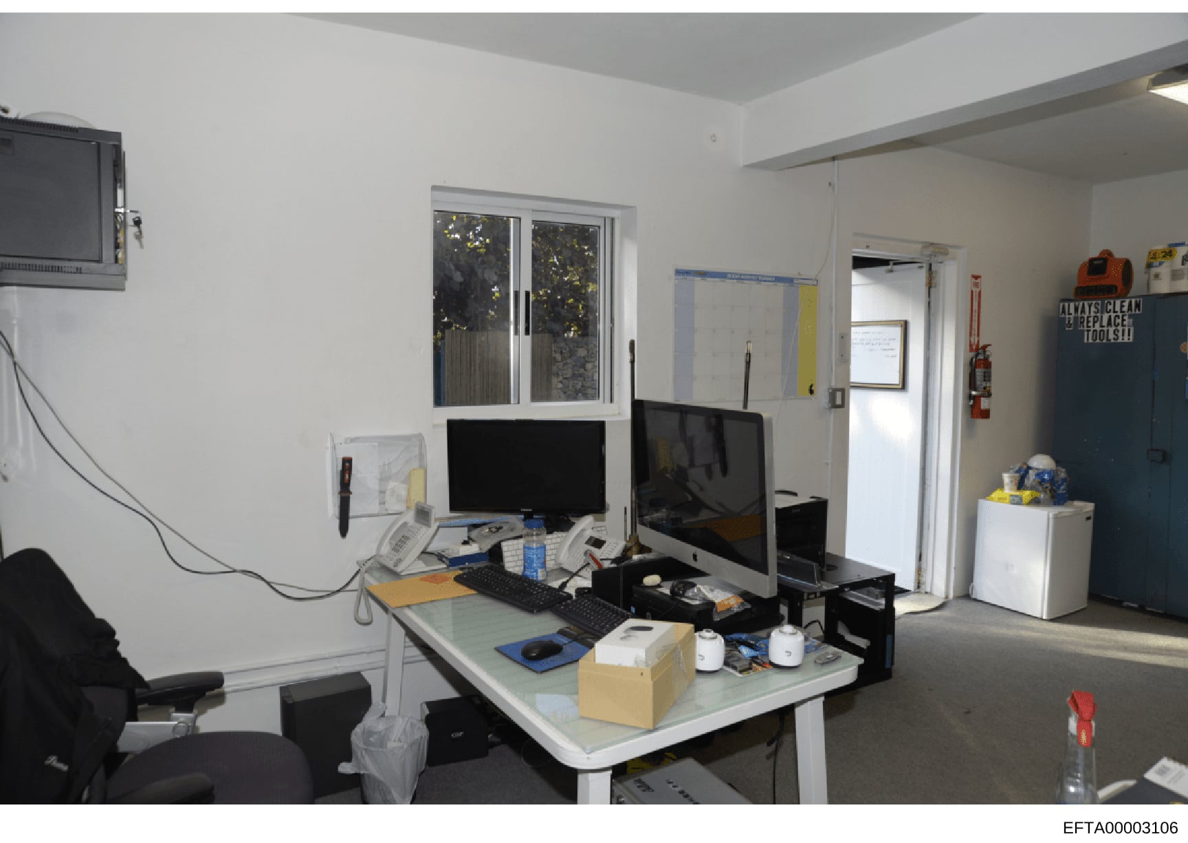 This is a photograph of a modern office or administrative workspace containing two computer monitors, desk equipment, and storage. The clean, minimalist white walls and organized layout suggest this may be an office used by Epstein's organization or 