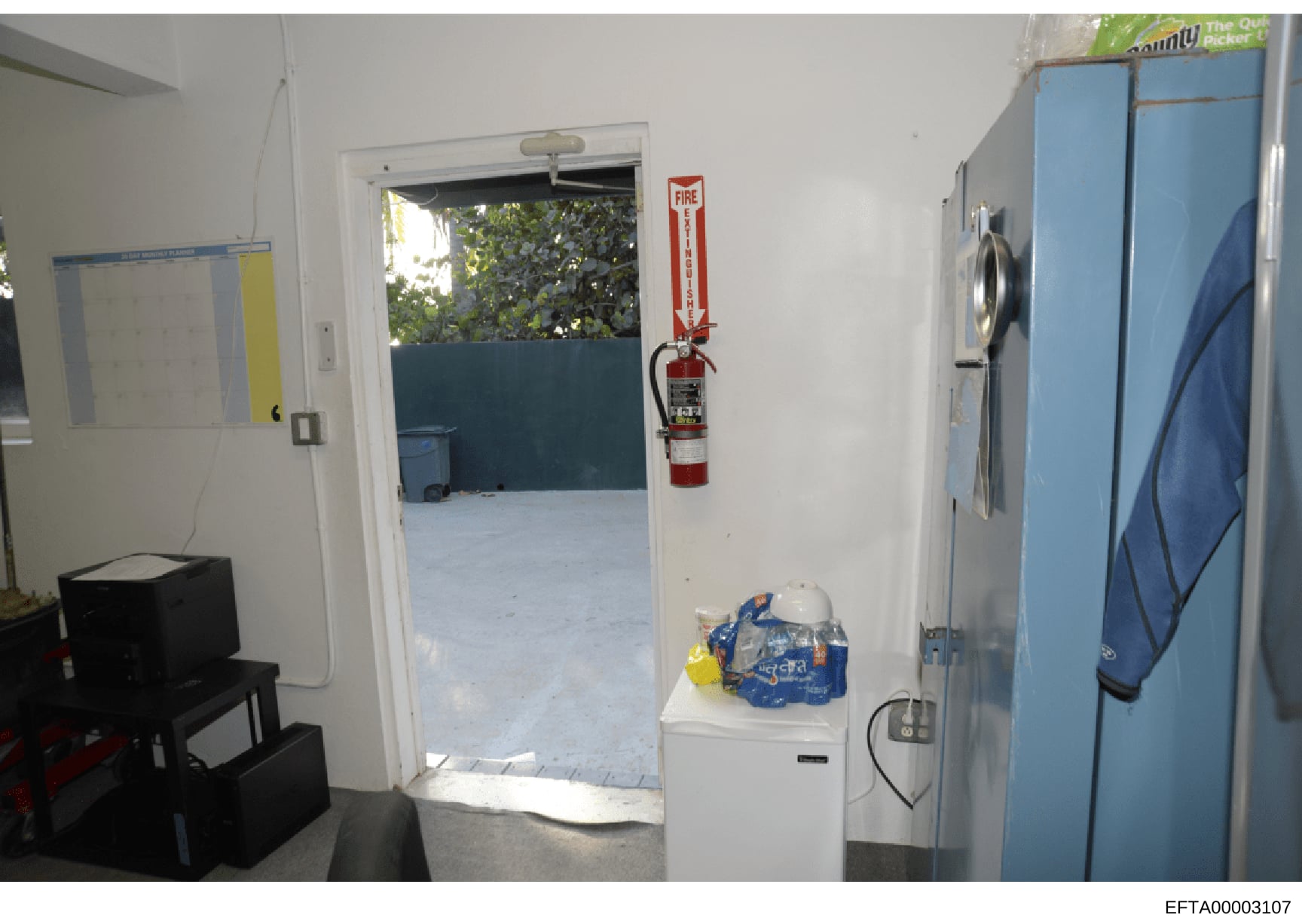 This is an evidence photograph showing the interior of a residential property, likely part of a location searched during the Epstein investigation. The image captures a doorway leading to an outdoor area, with visible fire safety equipment mounted on